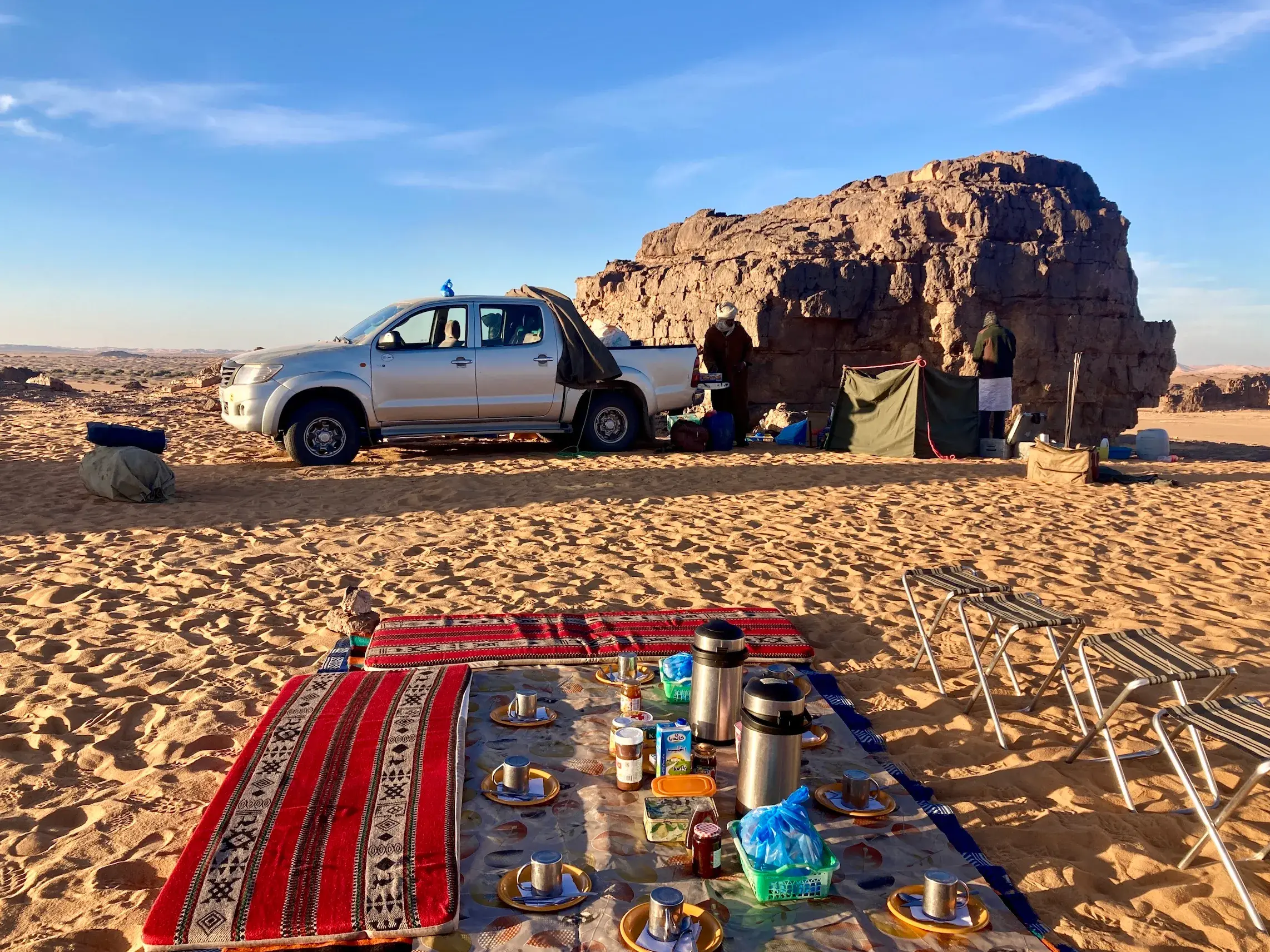 Authentische Mittagspause bei einer Trekkingtour in Algerien mit Picknickdecke und dem Tuareg-Begleitteam am Geländewagen.