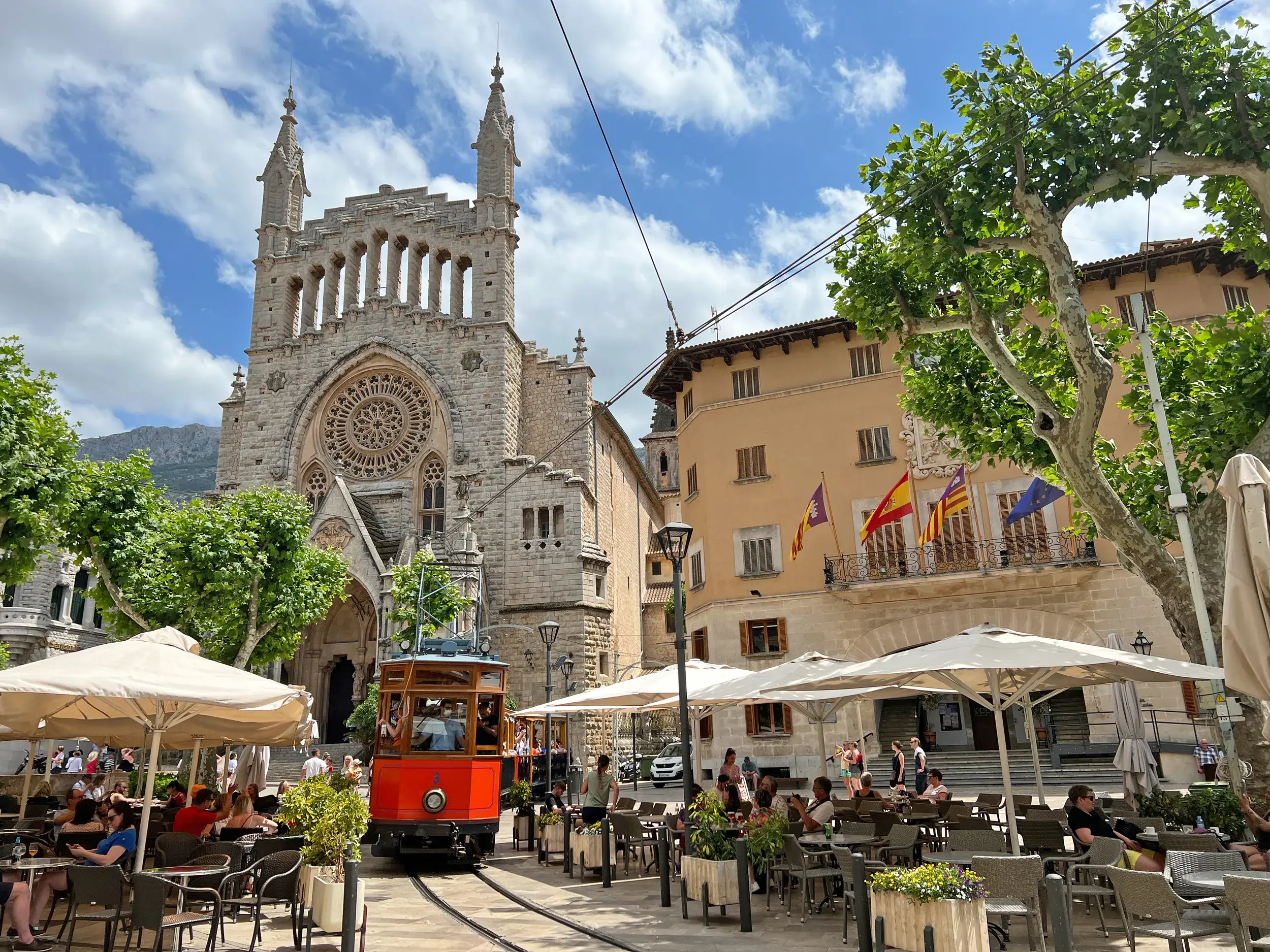 Die rote Nostalgiebahn von Sóller fährt am belebten Marktplatz vorbei an der Kirche Sant Bartomeu in der Serra de Tramuntana.