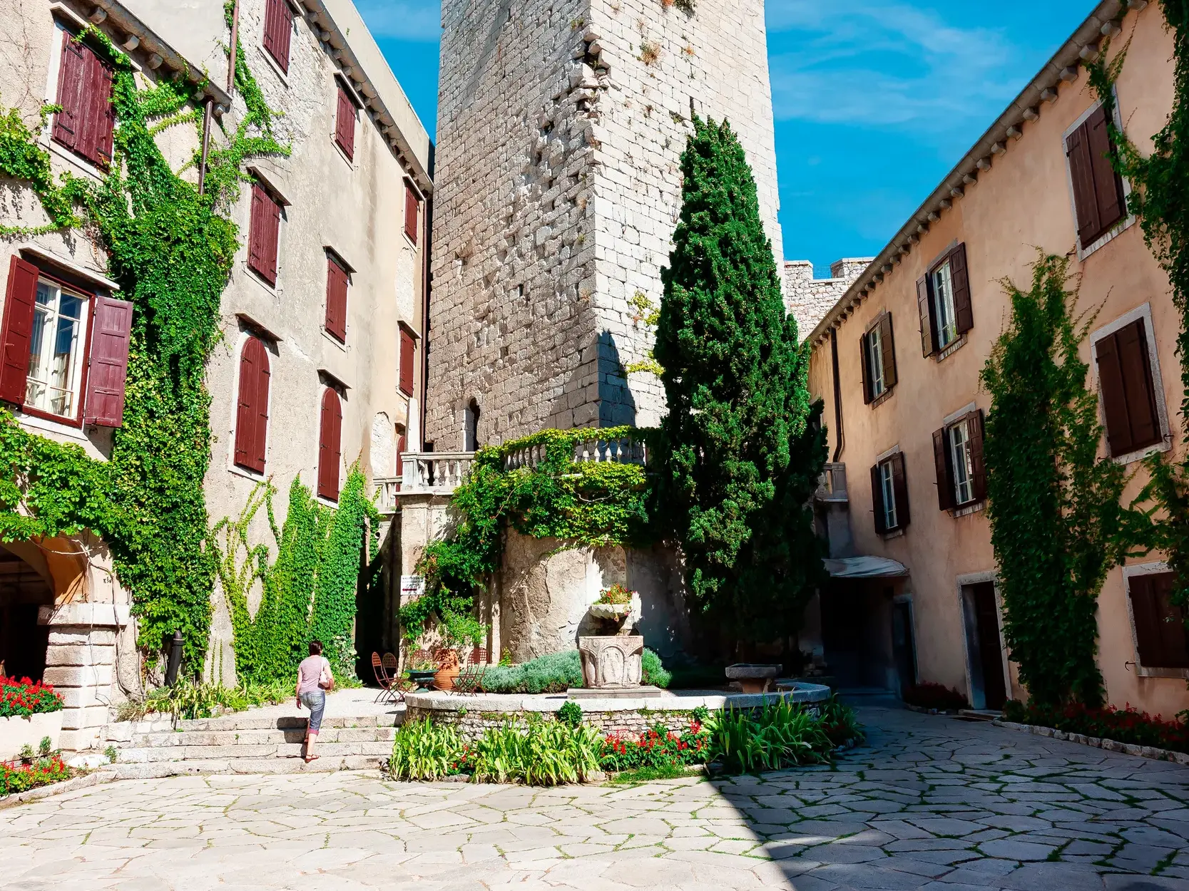 Sonniger, begrünter Innenhof des Hotels Cittar in der Altstadt von Novigrad mit historischem Turm und steinernem Brunnen.