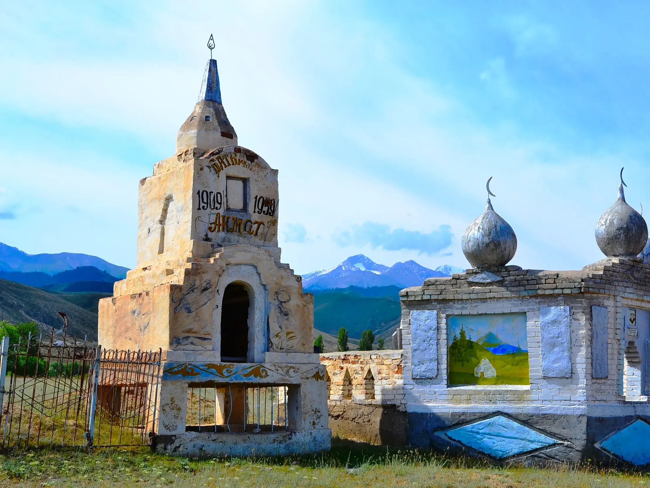 Zwei kunstvolle, historische Grabmäler auf einem Friedhof in Kirgistan, im Hintergrund die schneebedeckten Gipfel des Tian Shan.