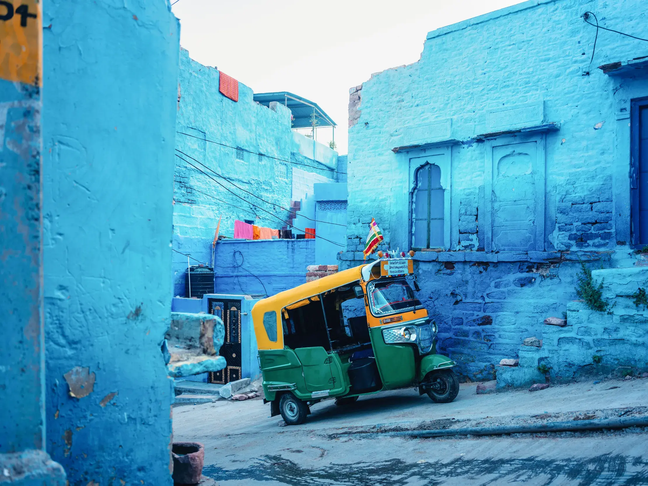 Ein buntes Tuk-Tuk parkt in einer engen Gasse, umgeben von den charakteristischen indigoblauen Häusern der Stadt Jodhpur.
