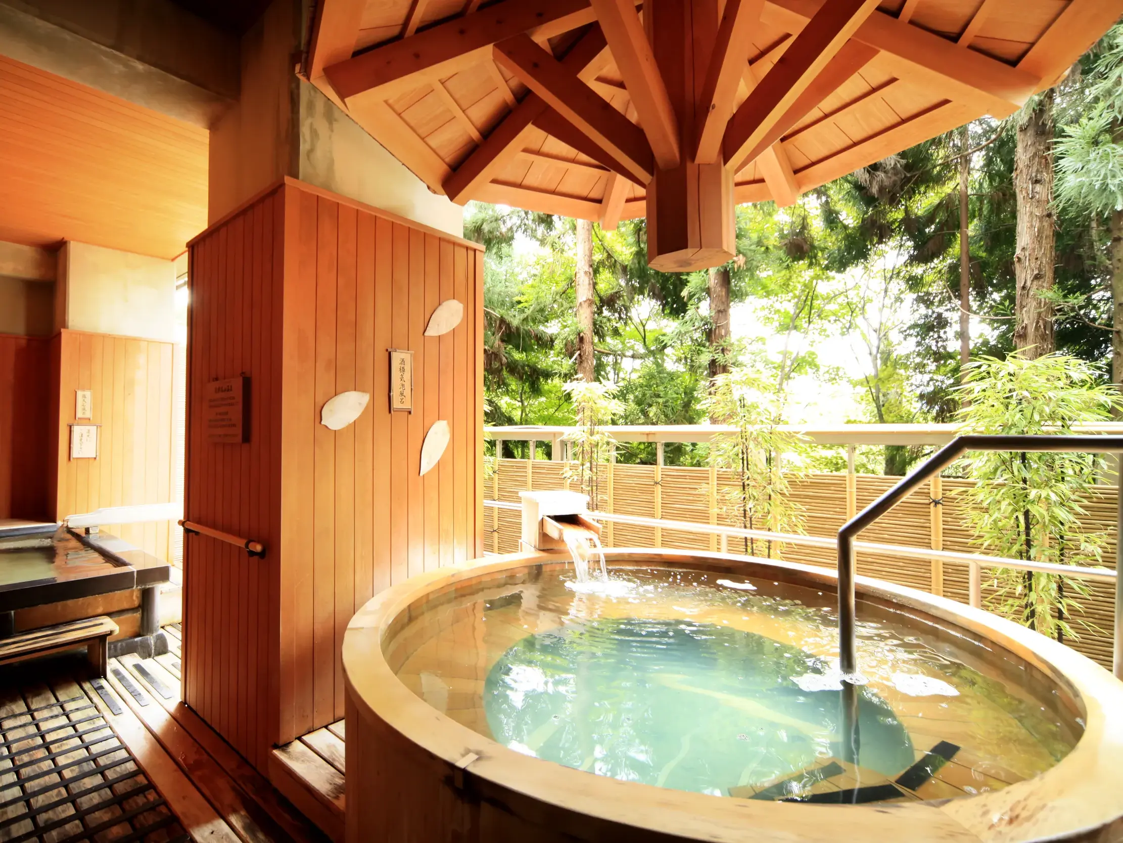 Traditionelles Onsen-Bad im Ryokan Hoshokaku in Takayama mit rundem Holzbottich und Blick in einen dichten Wald.