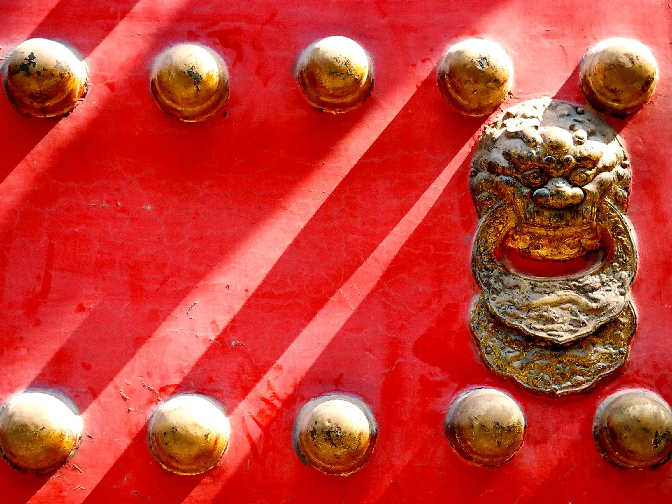 Detail eines traditionellen, roten Tores mit goldenem Löwenkopf-Türklopfer in der Verbotenen Stadt in Beijing.
