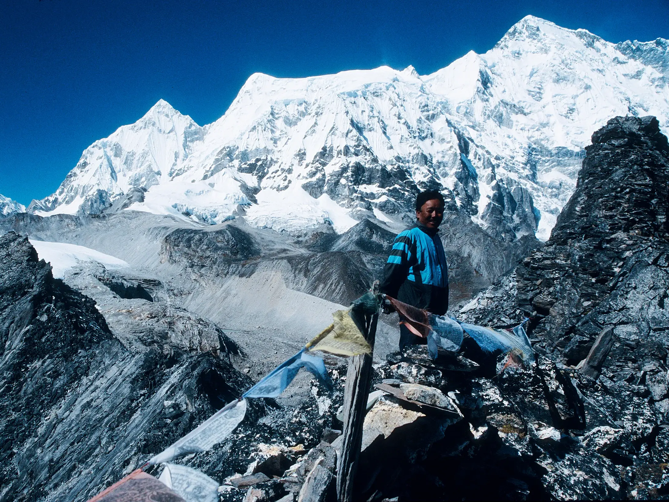 Einheimischer Guide steht auf dem Renjo La Pass in Nepal mit Gebetsfahnen und Blick auf die schneebedeckten Himalaya-Gipfel.
