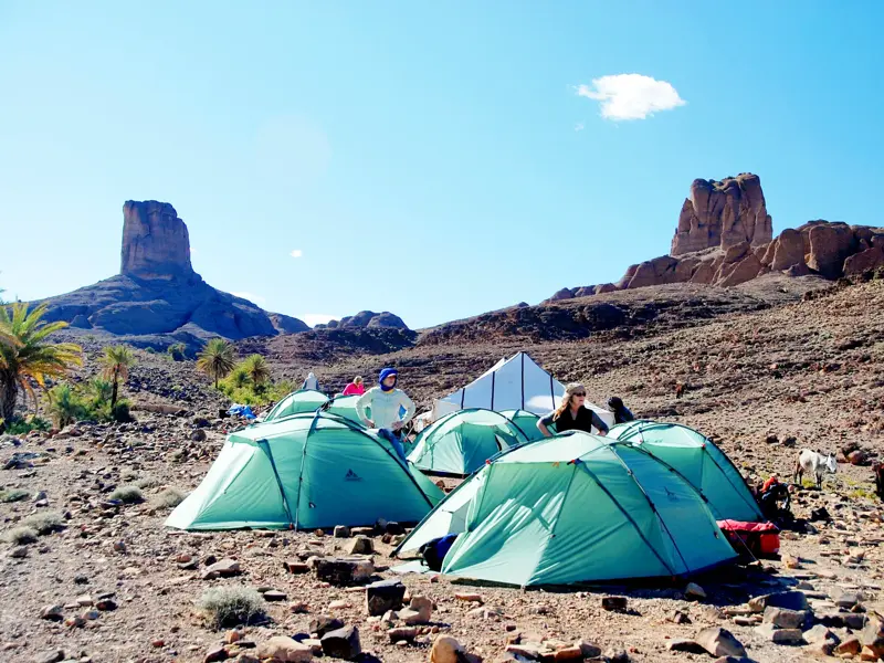 Aufgeschlagene Zelte einer Trekkinggruppe in der kargen Berglandschaft des Djebel Saghro mit den Felsentoren von Bab n'Ali.
