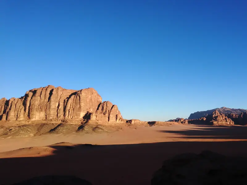 Ikonische Felsformationen erheben sich aus der weiten, roten Sandwüste des Wadi Rum in Jordanien unter klarem Himmel.