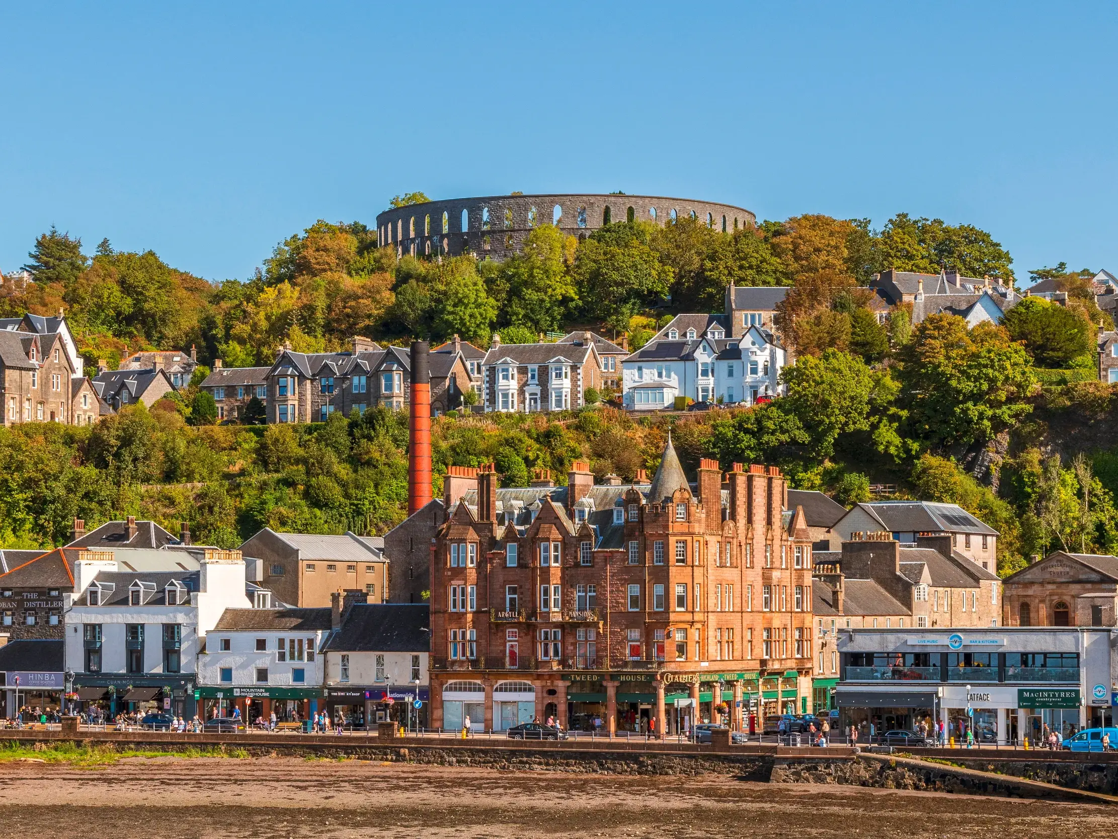 Malerische Ansicht der Hafenstadt Oban in Schottland mit der Promenade und dem McCaig's Tower bei strahlendem Sonnenschein.