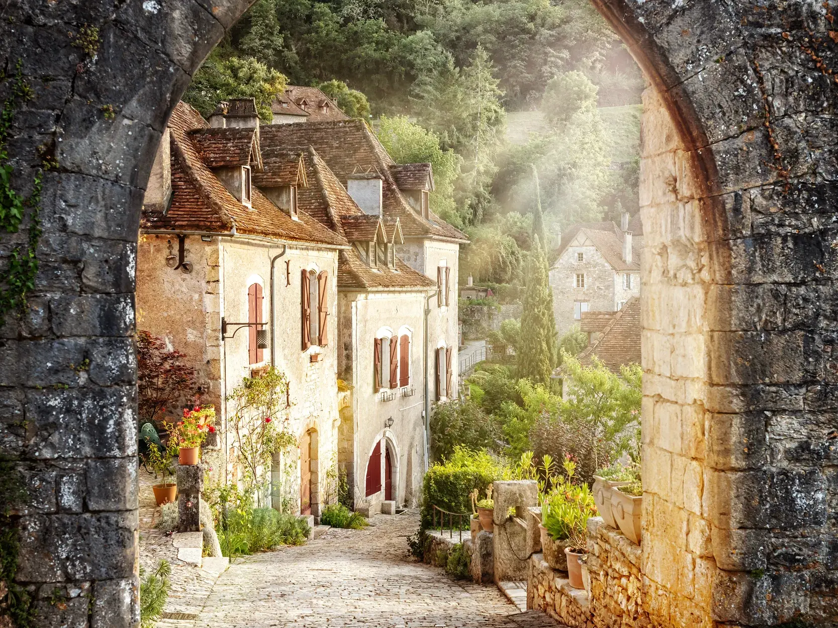 Stimmungsvoller Blick durch einen Torbogen auf eine Gasse mit alten Steinhäusern im malerischen Dorf St-Cirq-Lapopie.