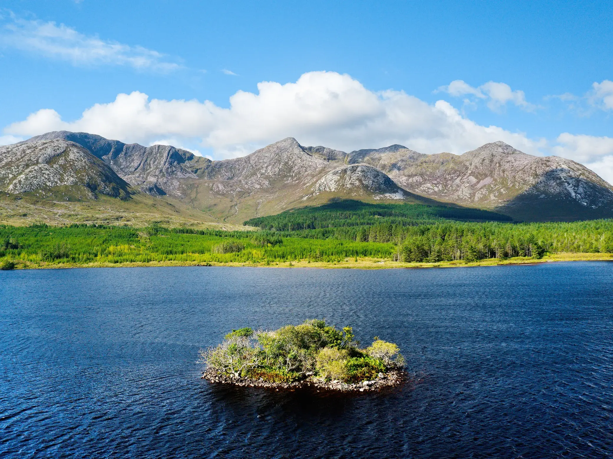 Kleine, baumbewachsene Insel im blauen Lough Inagh vor der majestätischen Bergkette der Twelve Bens in Connemara, Irland.