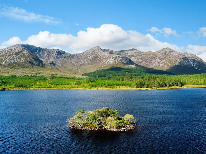 Kleine, baumbewachsene Insel im blauen Lough Inagh vor der majestätischen Bergkette der Twelve Bens in Connemara, Irland.