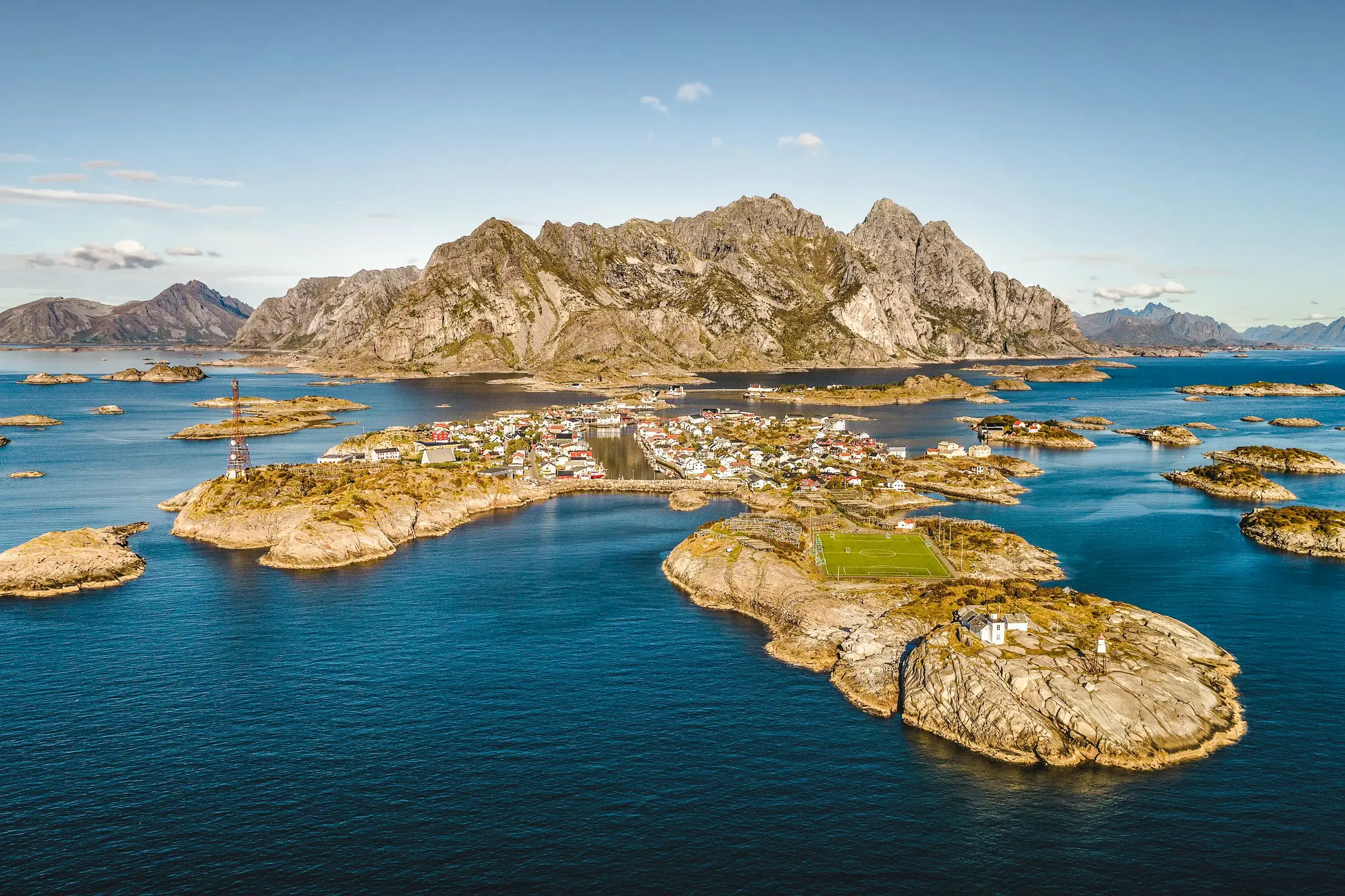 Blick auf das Fischerdorf Henningsvær auf der Insel Austvågøya mit dem berühmten Fußballplatz vor der Bergkulisse der Lofoten.