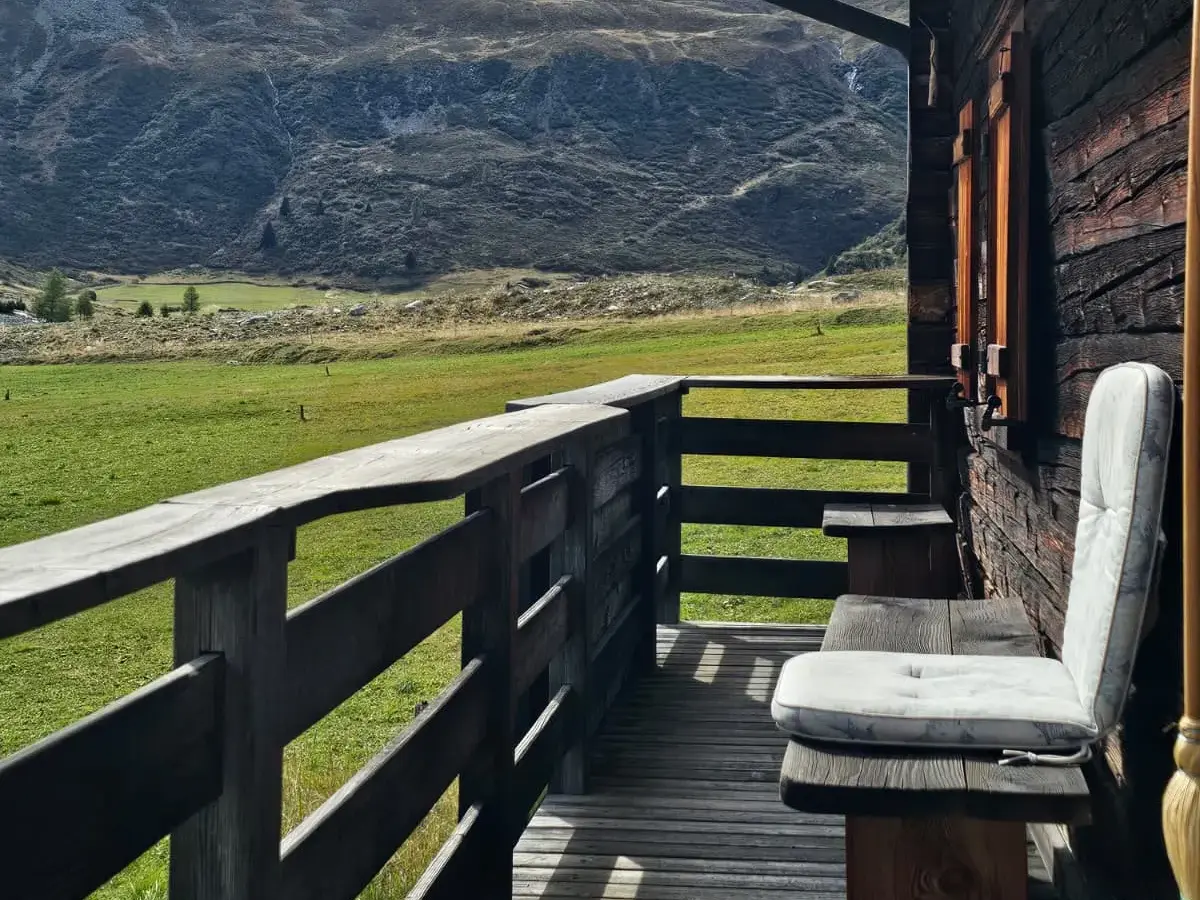 Einladender Holzbalkon mit Sitzbank bietet einen weiten Blick über grüne Bergwiesen auf die Alpengipfel von Graubünden bei Bivio.