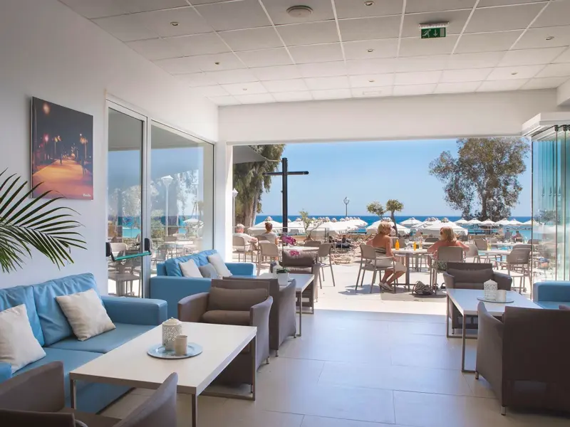 Helle Lobby im Hotel Harmony Bay mit bequemen Sofas und freiem Blick auf die Sonnenterrasse und den Strand von Limassol.