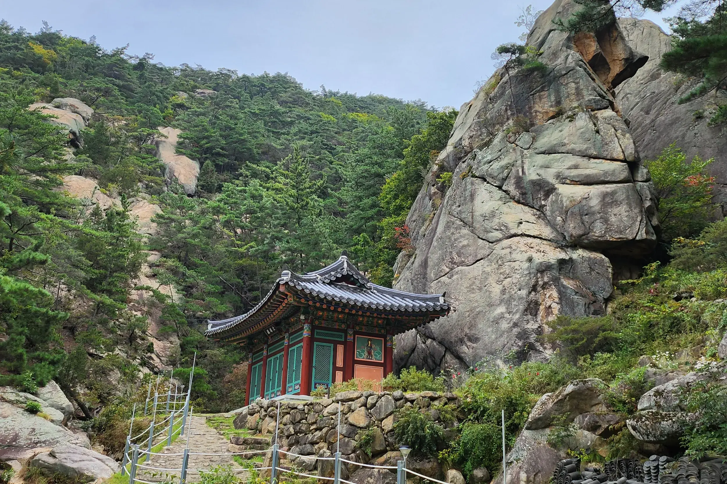 Ein traditioneller koreanischer Tempel am steinernen Wanderweg auf den Gyeongju Namsan, umgeben von Felsen und Wäldern.