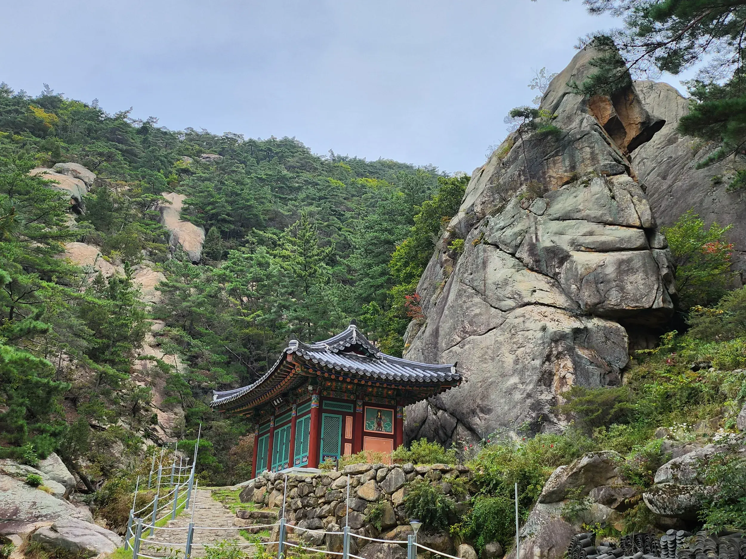 Ein traditioneller koreanischer Tempel am steinernen Wanderweg auf den Gyeongju Namsan, umgeben von Felsen und Wäldern.