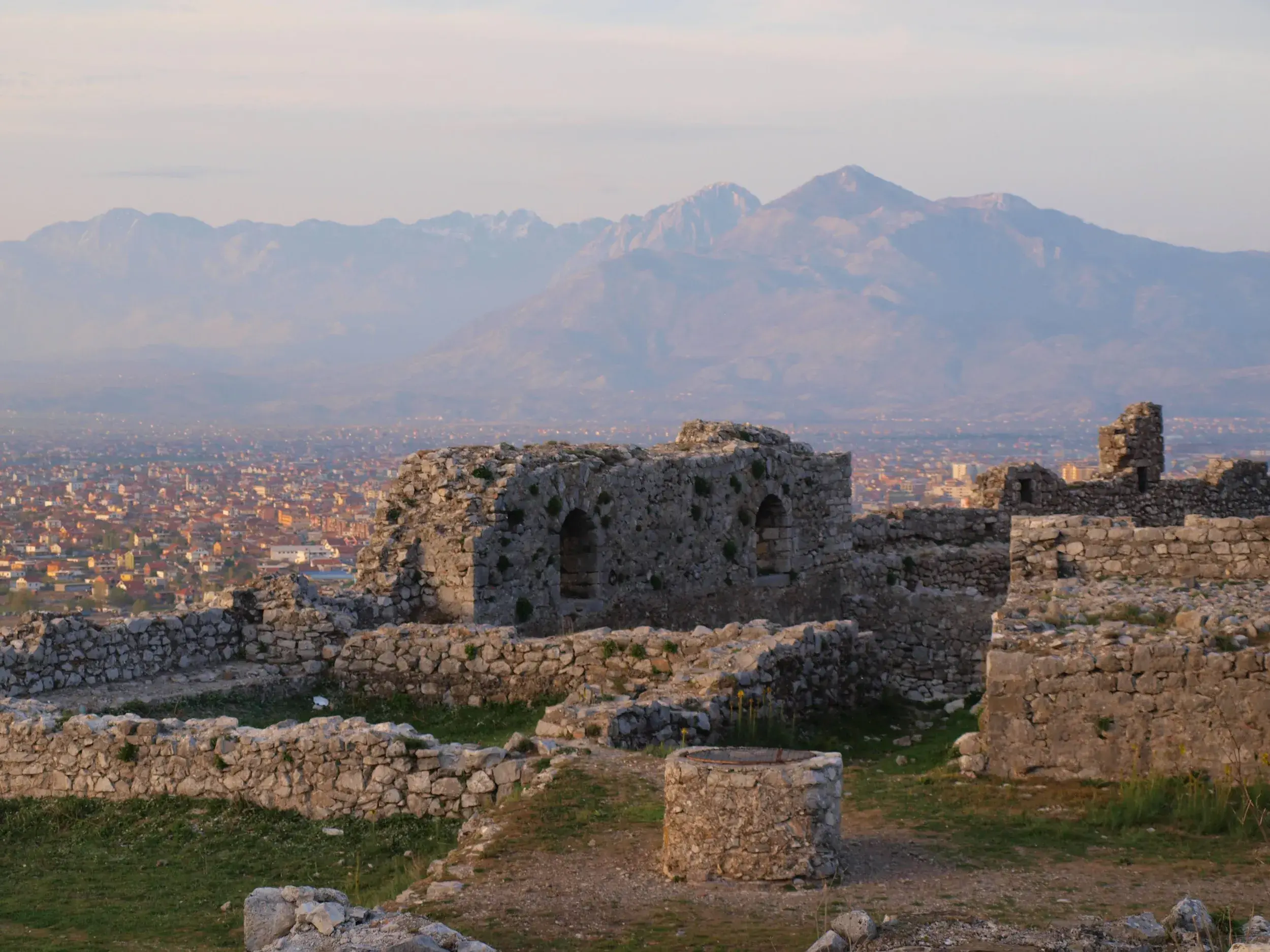 Historische Steinruinen der Burg Rozafa mit Blick über die Stadt Shkodra auf die albanischen Alpen im Abendlicht.
