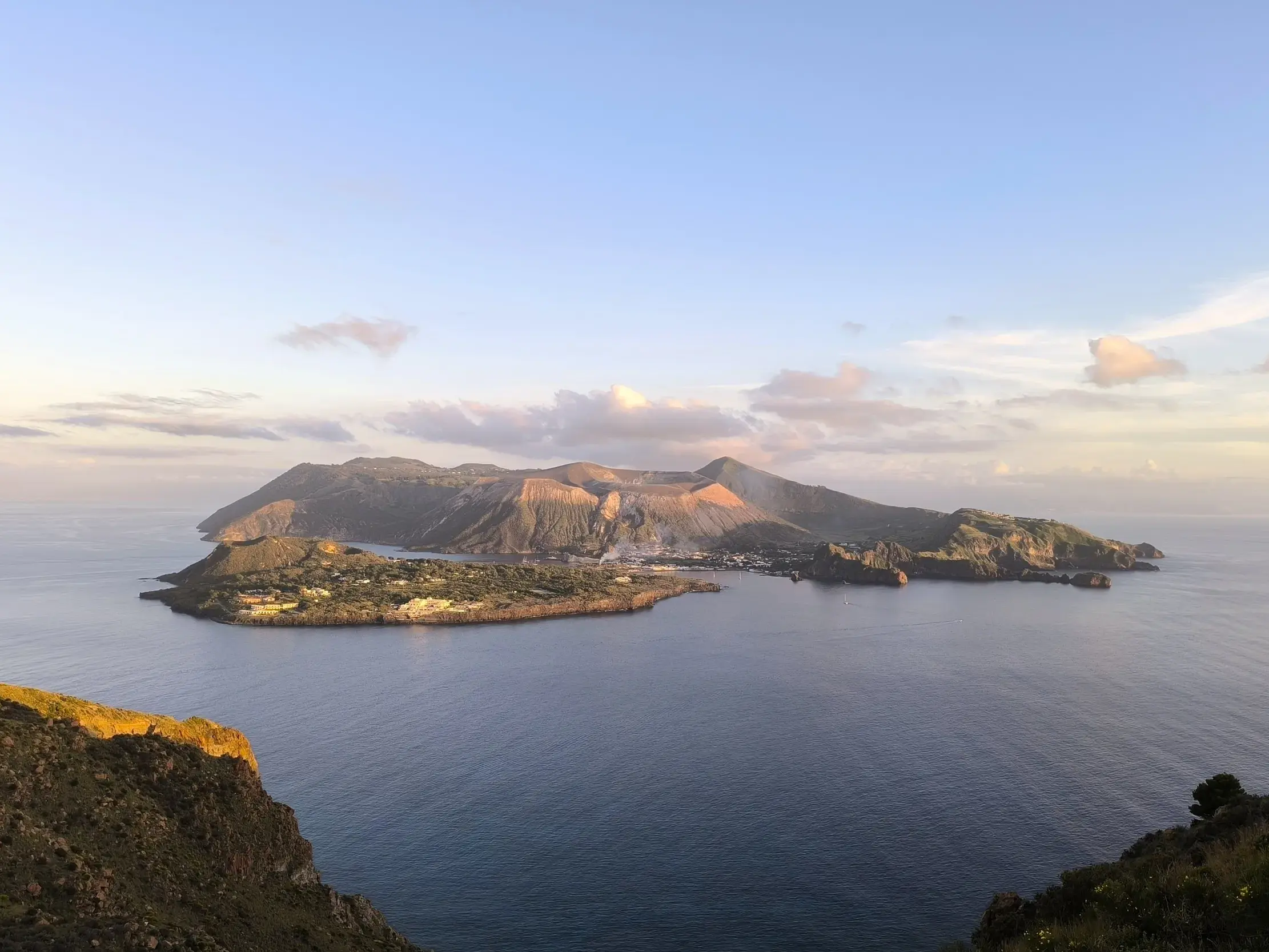 Panoramablick von einem Wanderweg auf die Vulkaninsel Vulcano mit dem Gran Cratere im warmen Abendlicht, umgeben vom Meer.