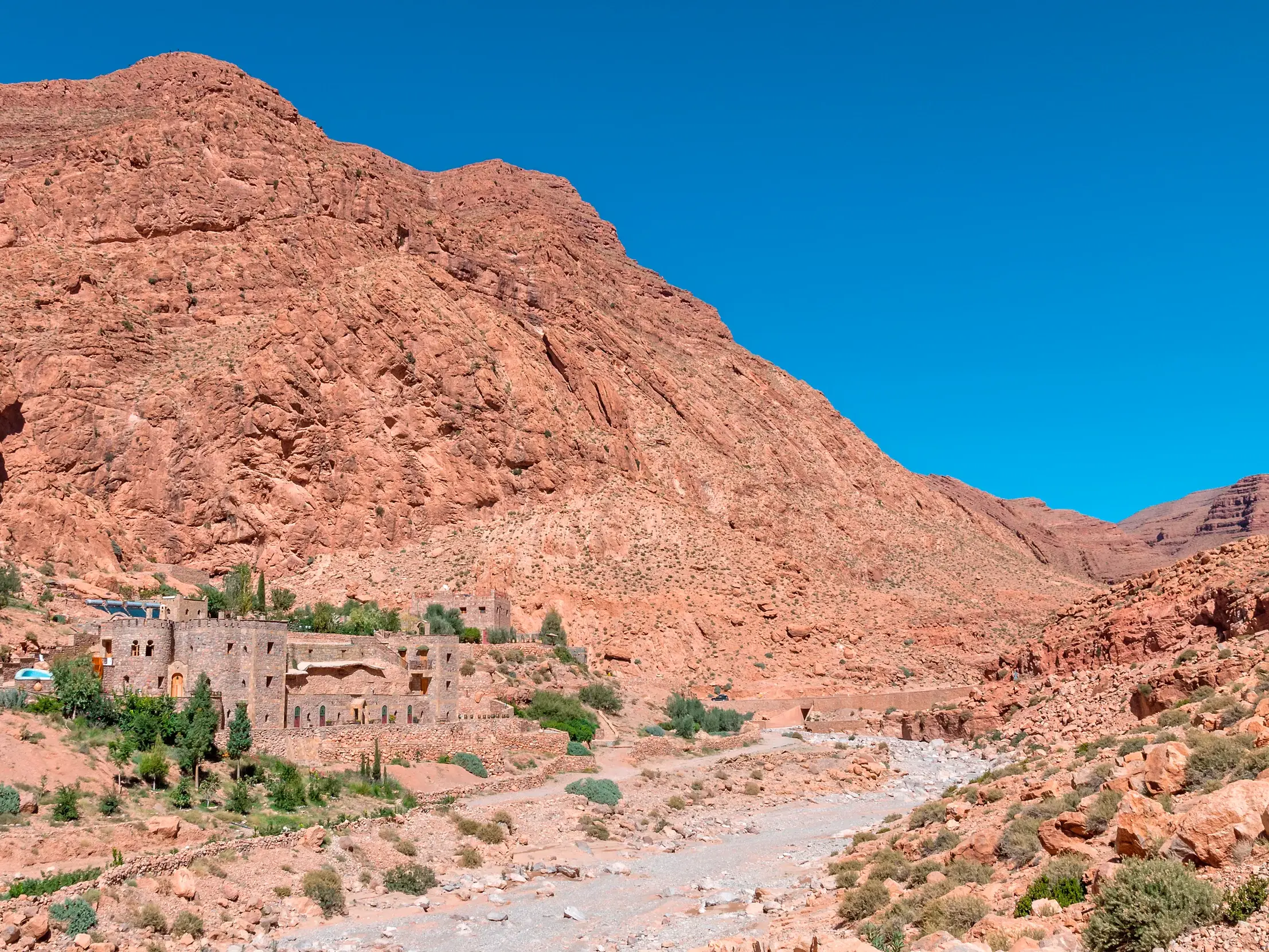Eine traditionelle Lehm-Kasbah schmiegt sich an die imposanten roten Felsen der Todraschlucht in Marokko.