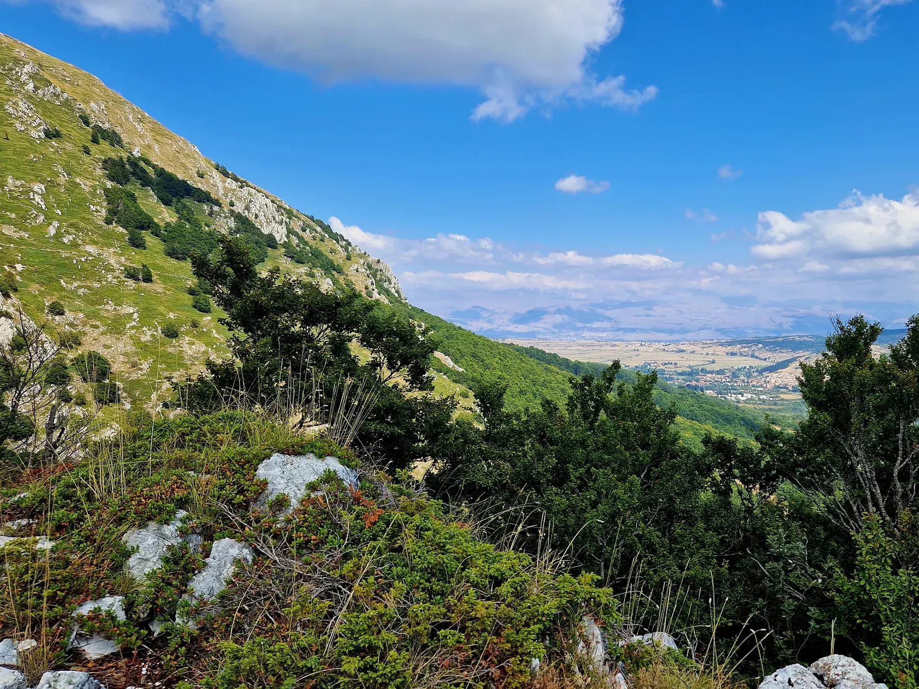 Weite Aussicht beim Wandern im Sirente-Velino-Regionalpark über die grüne Berglandschaft des Apennin auf die Fuciner Hochebene.