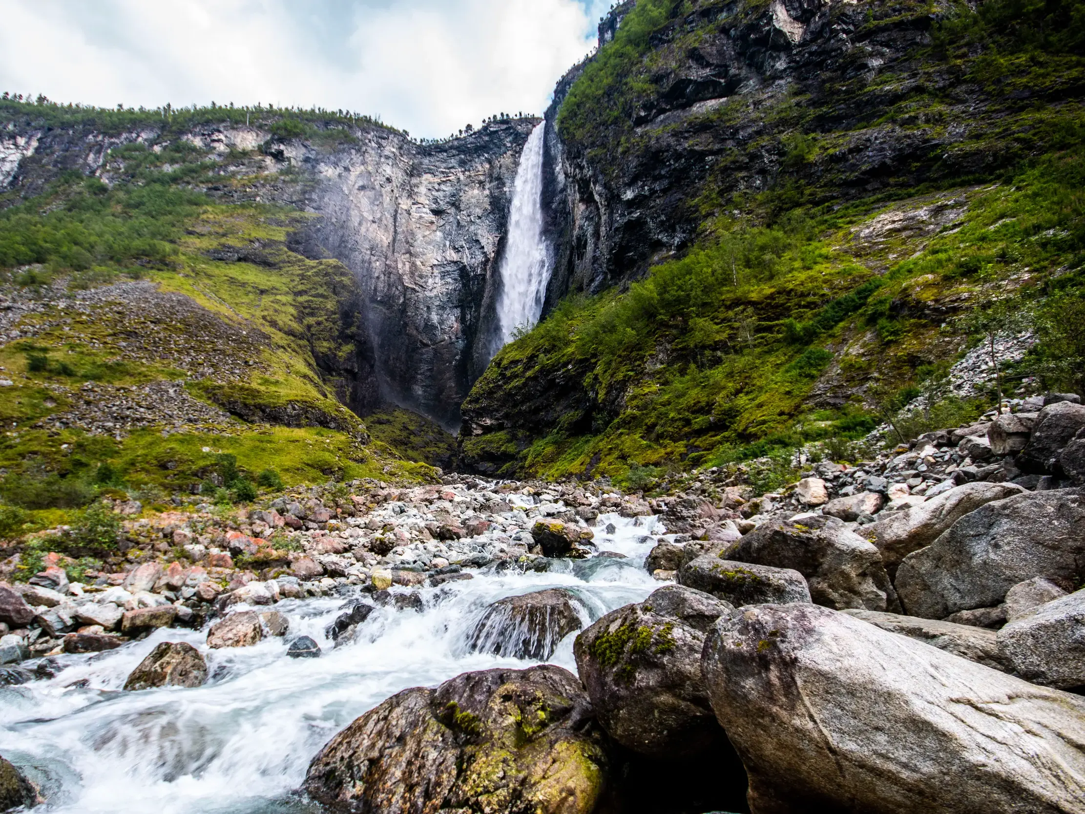 Mächtiger Vettisfossen Wasserfall im Utladalen stürzt eine bemooste Felswand hinab in einen reißenden Gebirgsfluss.