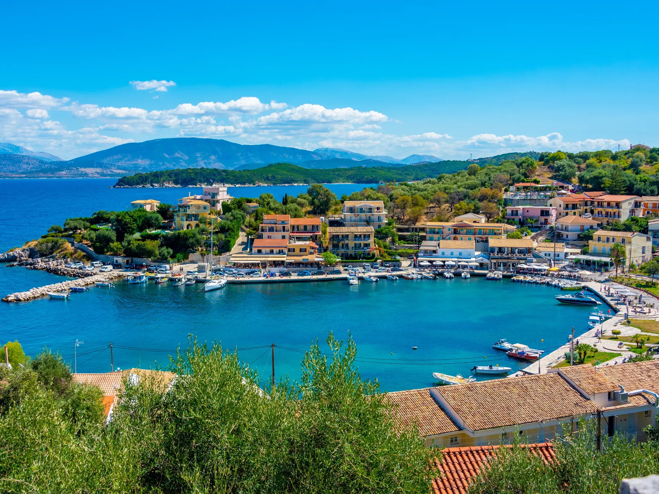 Blick von oben auf die hübsche Hafenpromenade von Kassiopi mit Booten in der türkisfarbenen Bucht auf der Wanderinsel Korfu.