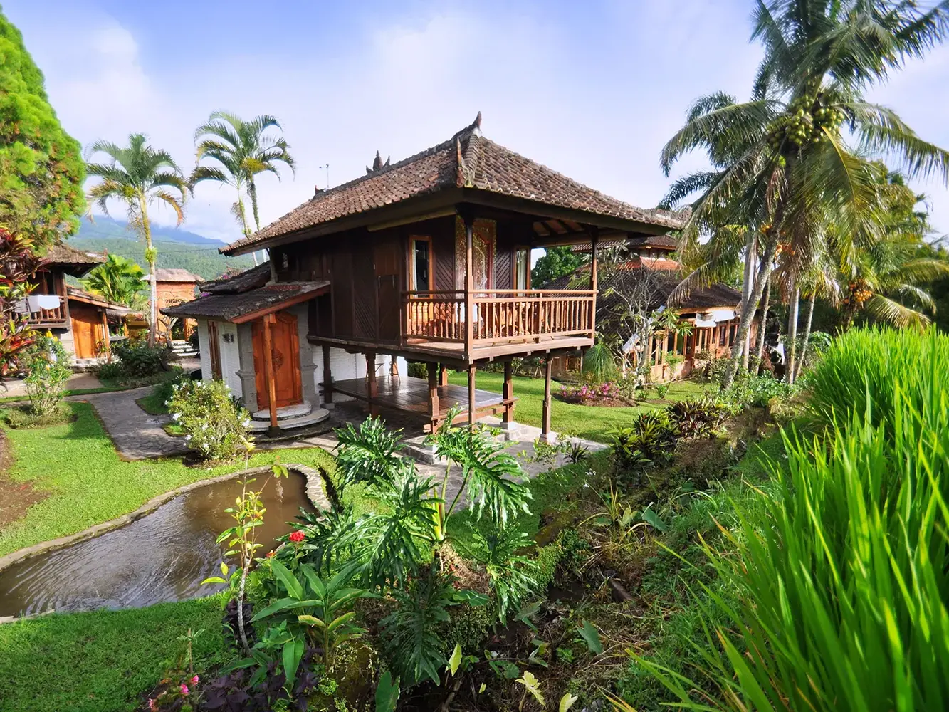 Holzbungalow auf Stelzen im idyllischen Resort Puri Lumbung in Munduk, Bali, eingebettet in grüne Reisterrassen und Palmen.