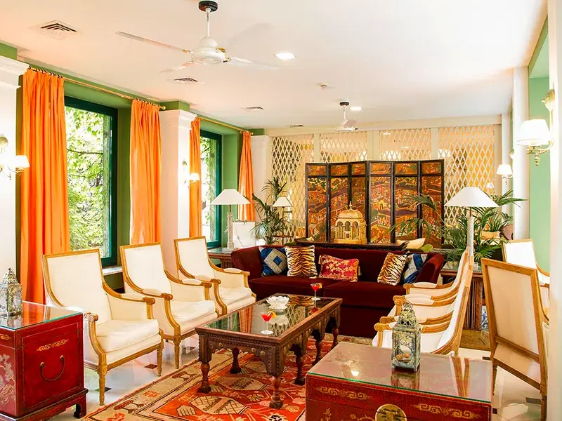 Eleganter Salon im Hotel Victoria in Turin mit rotem Sofa, weißen Sesseln, orangefarbenen Vorhängen und asiatischen Akzenten.