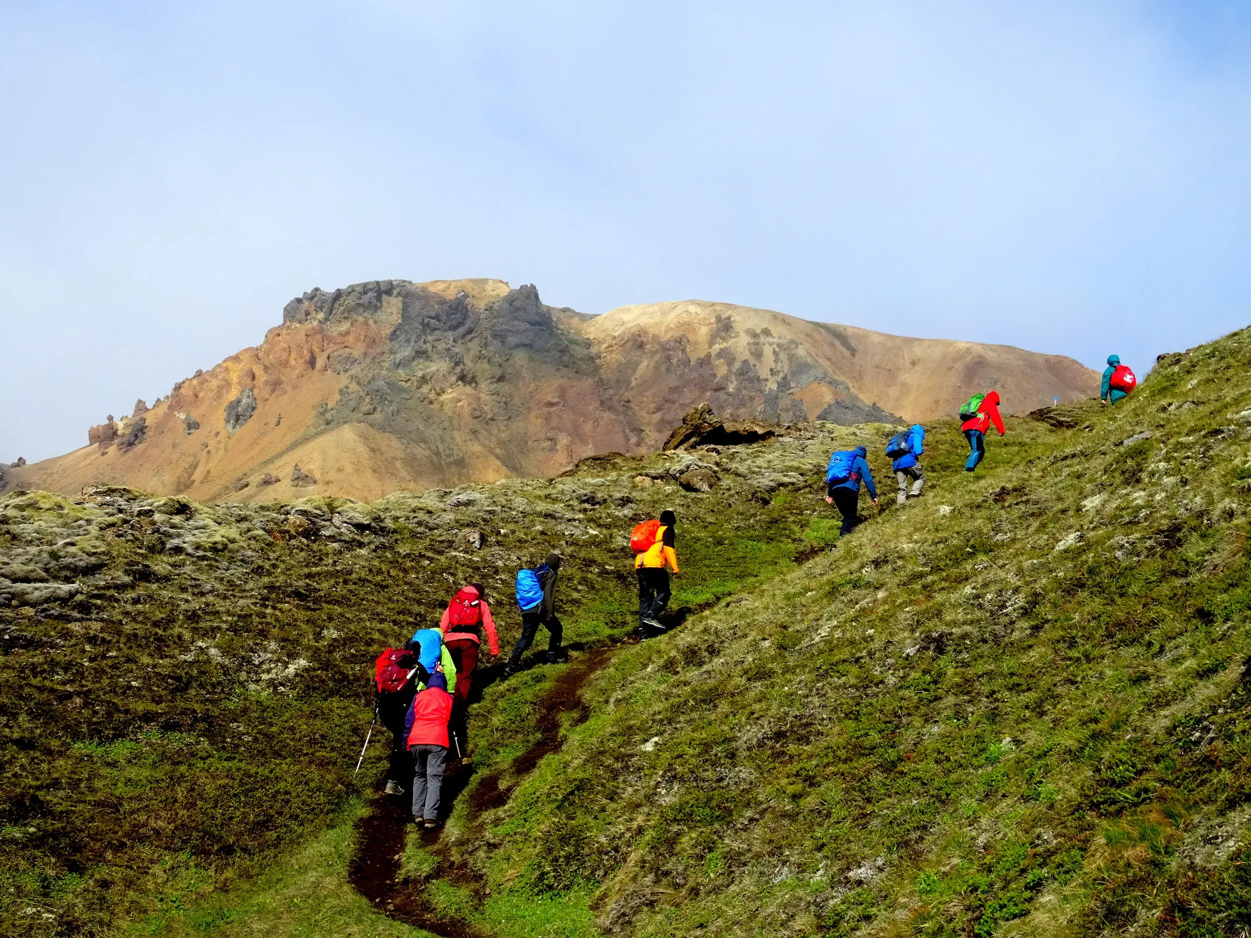 Wandergruppe in bunten Jacken besteigt den Berg Brennisteinsalda in der farbenfrohen Vulkanlandschaft von Landmannalaugar.