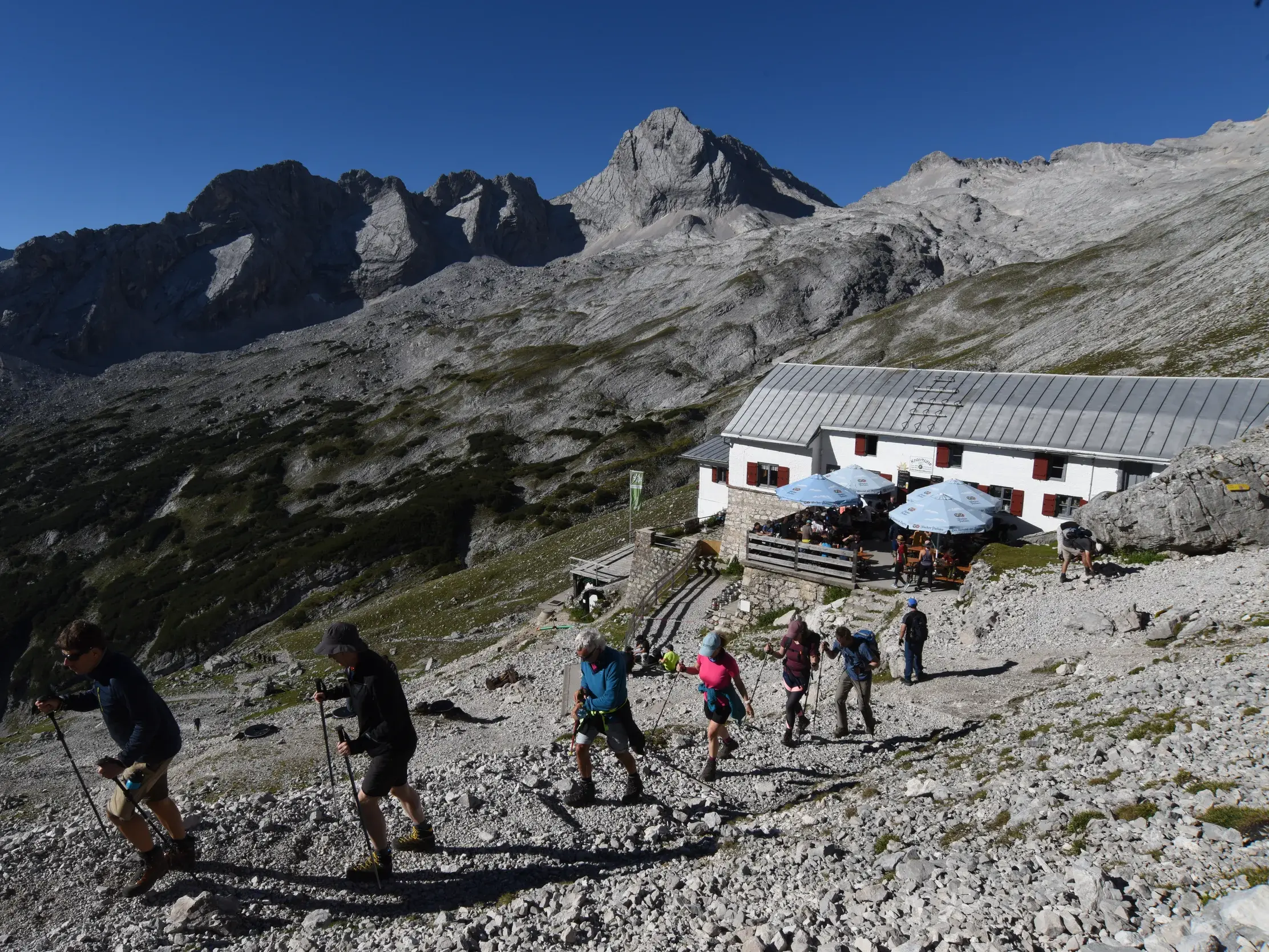 Wandergruppe bei der Bergwanderung auf einem Geröllweg zur Knorrhütte mit der Felskulisse des Zugspitzplatts im Hintergrund.