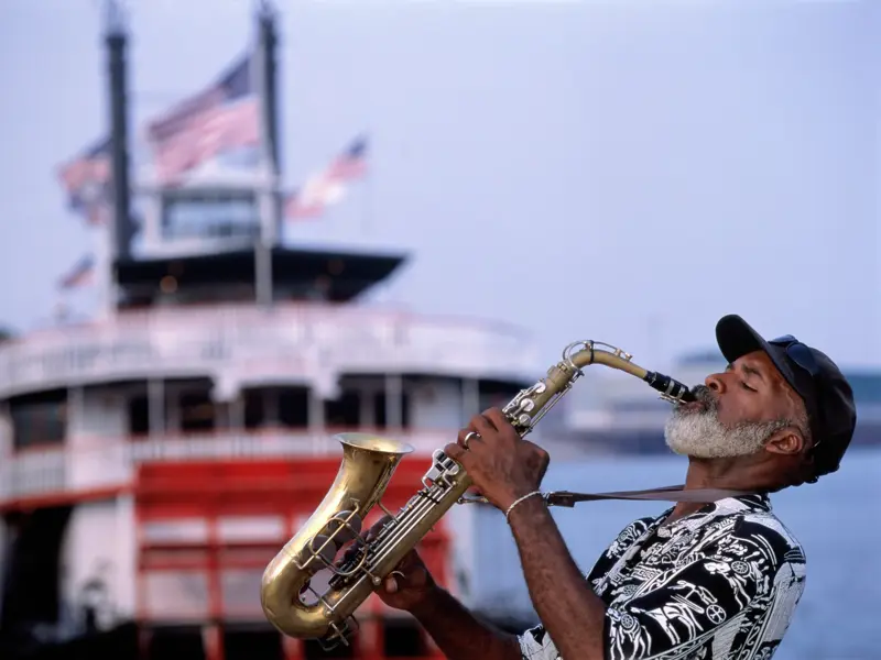 Ein Jazz-Saxofonist spielt mit Leidenschaft vor einem historischen Schaufelraddampfer auf dem Mississippi in New Orleans.