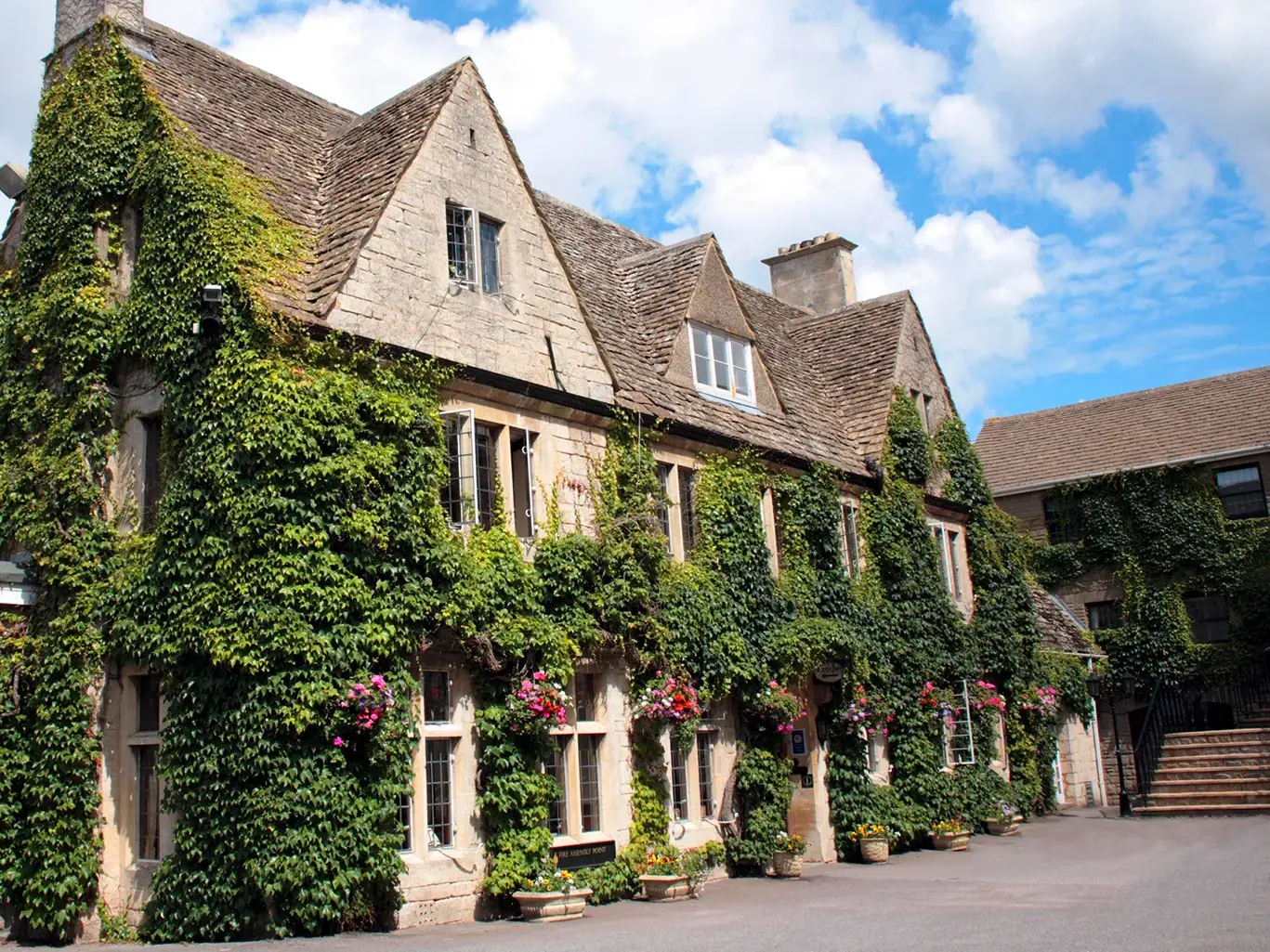 Efeubewachsene Steinfassade des charmanten Landhotels Hatton Court in Südengland an einem sonnigen Tag mit blauem Himmel.