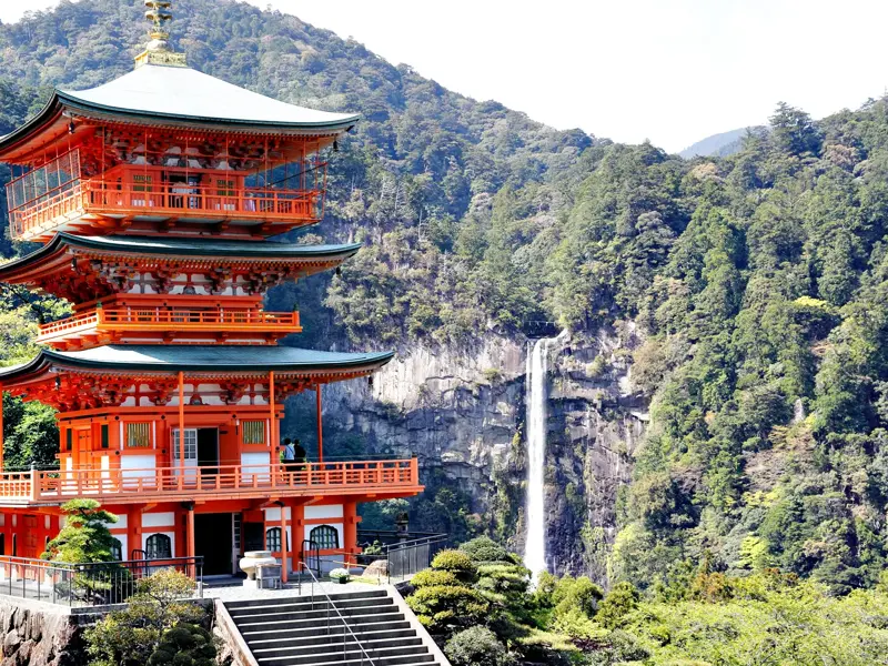 Die rote Seiganto-ji Pagode vor dem tosenden Nachi-Wasserfall in den bewaldeten Bergen der Kii-Halbinsel in Japan.