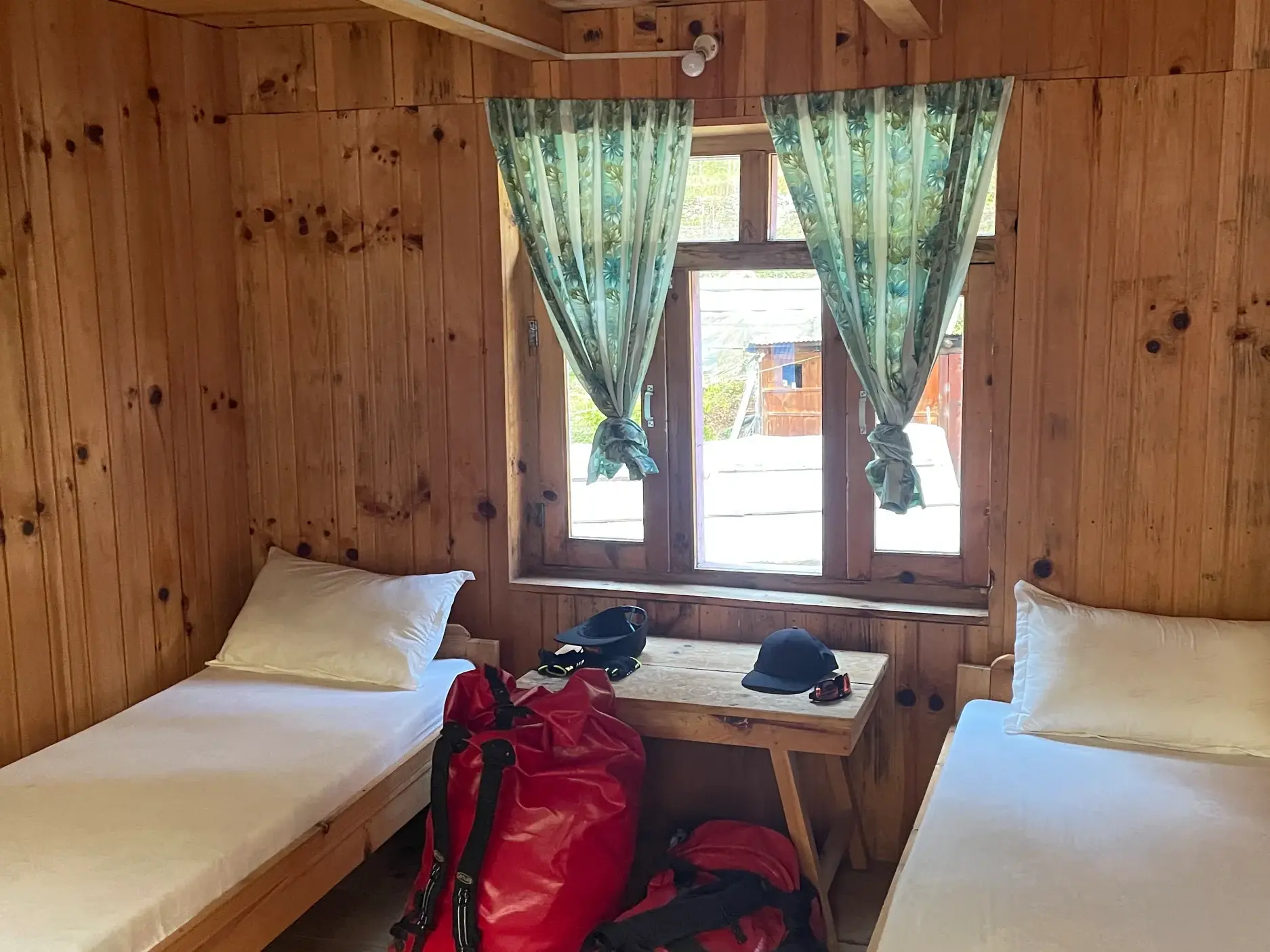 Innenansicht einer holzgetäfelten Lodge-Unterkunft mit zwei Einzelbetten und Trekking-Gepäck während der Manaslu-Runde.