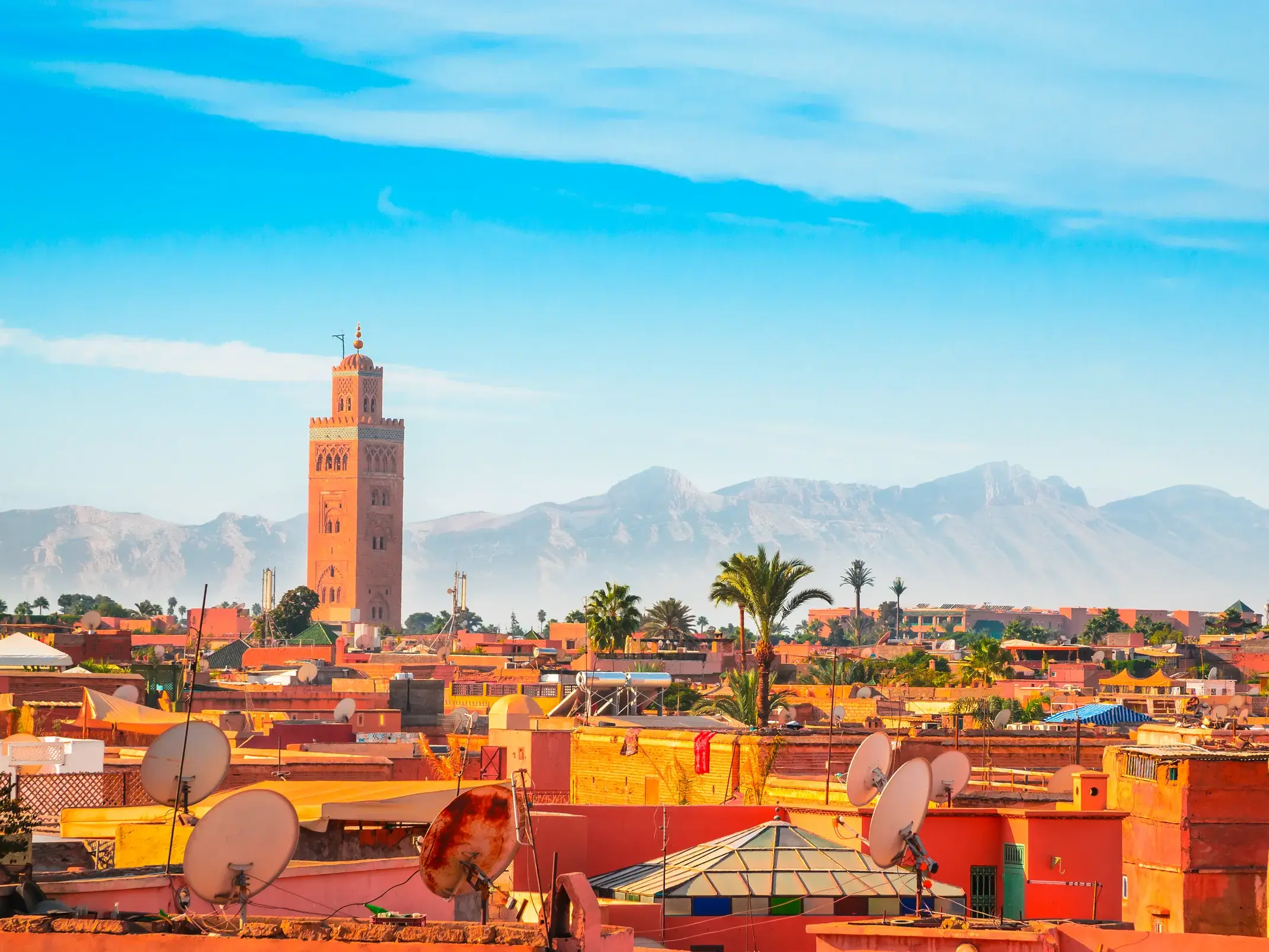 Panoramablick auf die Koutoubia-Moschee und die Dächer von Marrakesch, mit dem Atlasgebirge am Horizont.