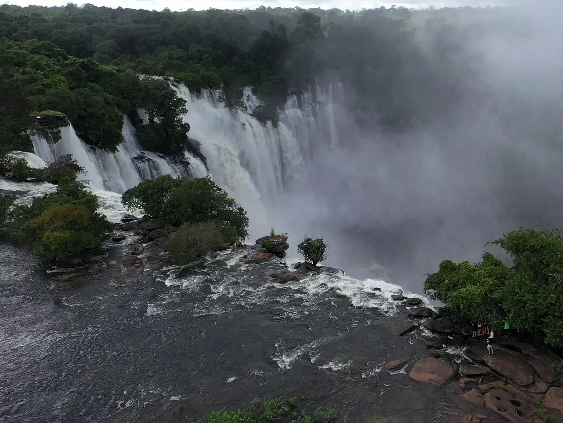 Reisegruppe bestaunt die gewaltigen, nebelverhangenen Kalandula Wasserfälle in Angola von einer Felskante am Lucala-Fluss aus.