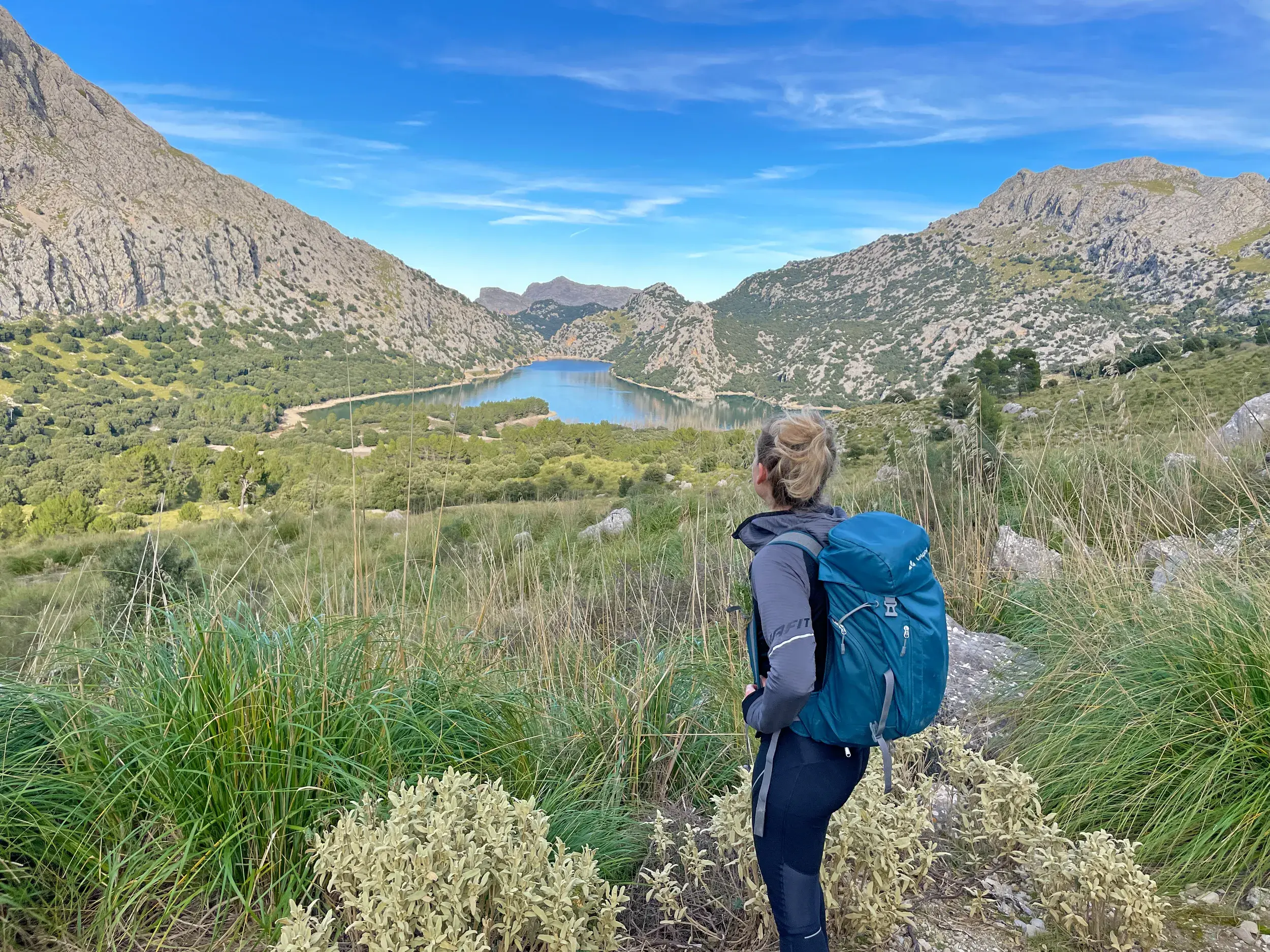 Wanderin mit Rucksack genießt auf einer Anhöhe den Panoramablick auf den Cuber Stausee in der Serra de Tramuntana.