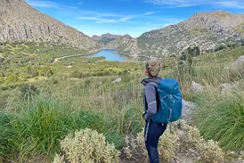 Wanderin mit Rucksack genießt auf einer Anhöhe den Panoramablick auf den Cuber Stausee in der Serra de Tramuntana.