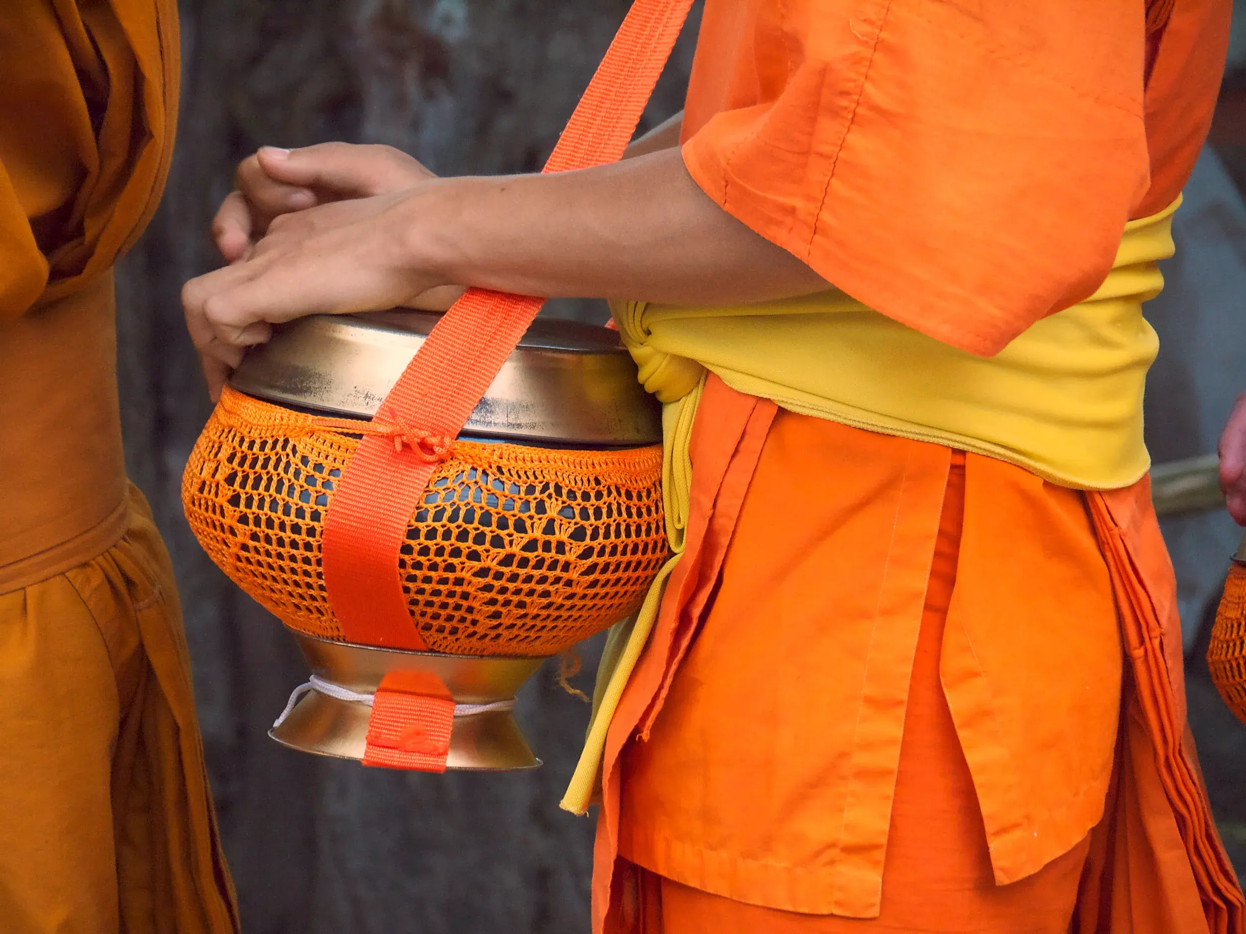 Nahaufnahme eines Mönchs in oranger Robe, der auf einer Kleingruppenreise in Luang Prabang seine Almosenschale trägt.