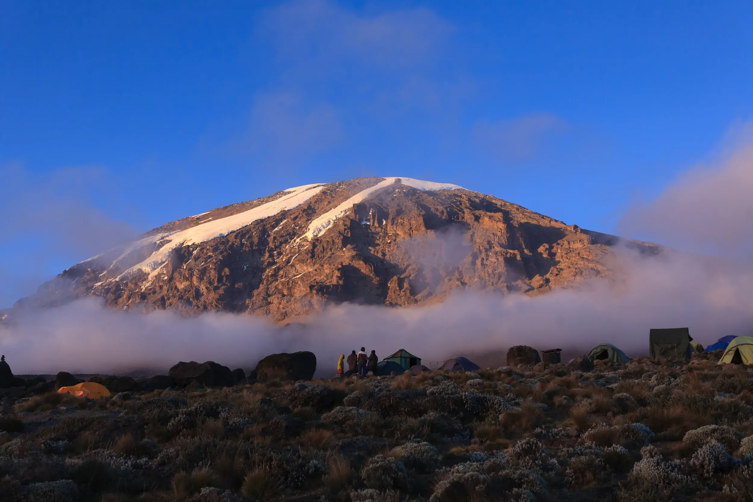 Zeltlager einer Trekking-Gruppe am Kilimanjaro mit Blick auf den sonnenbeschienenen Kibo-Gipfel über den Wolken.