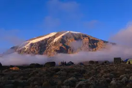Zeltlager einer Trekking-Gruppe am Kilimanjaro mit Blick auf den sonnenbeschienenen Kibo-Gipfel über den Wolken.