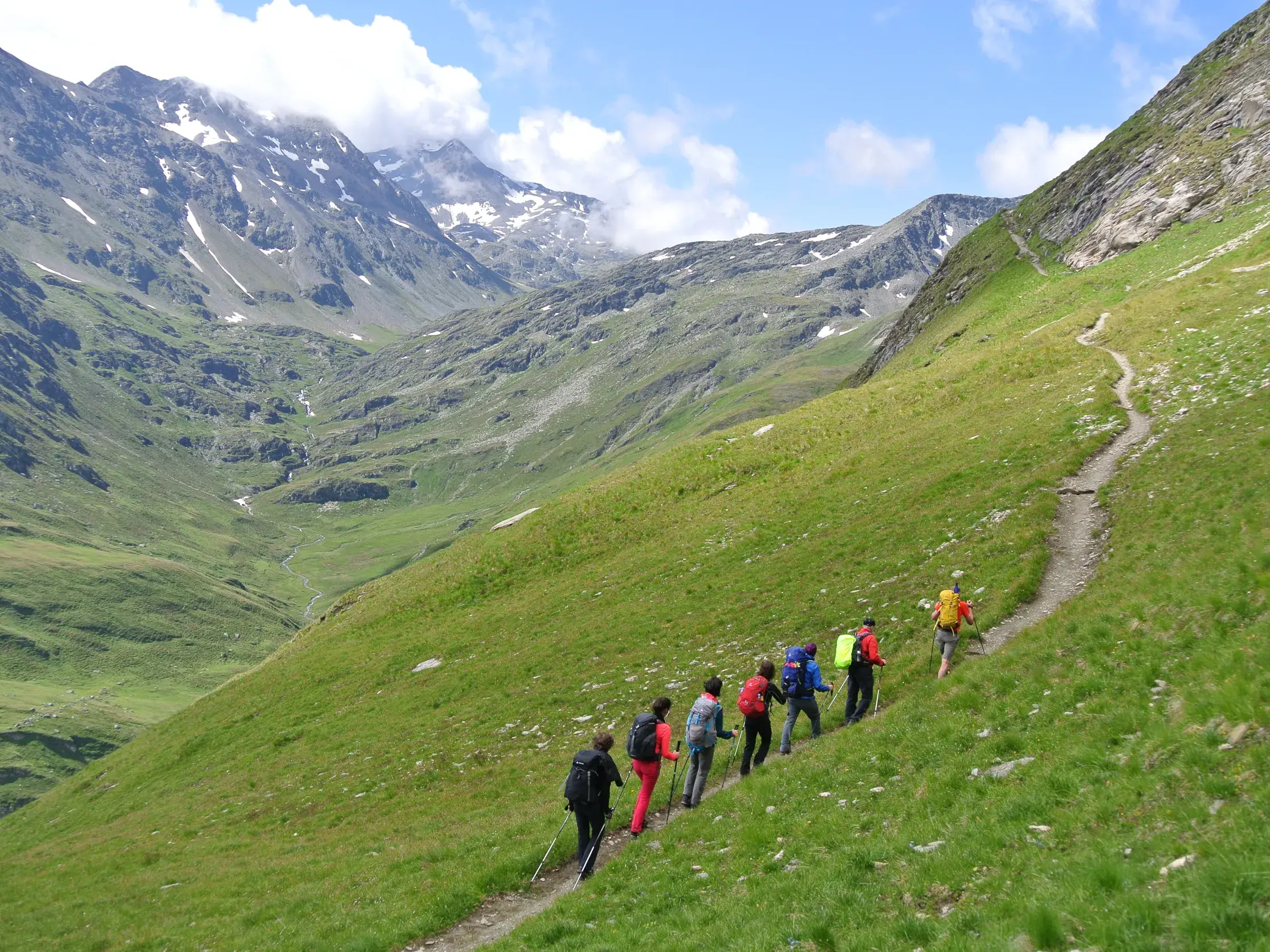 Eine Wandergruppe mit Rucksäcken auf einem schmalen Bergpfad während der Glocknerrunde im Nationalpark Hohe Tauern.