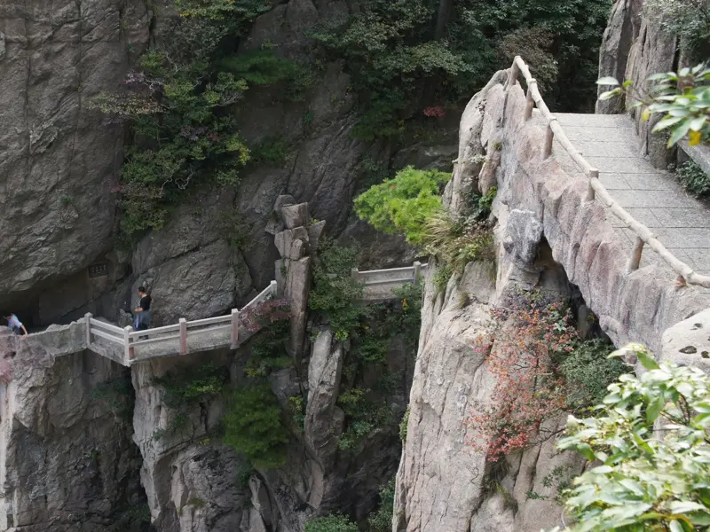 Wanderer auf einem spektakulären, in die Felswand gehauenen Weg im Huang Shan Gebirge, einer Station der Trekkingreise in China.