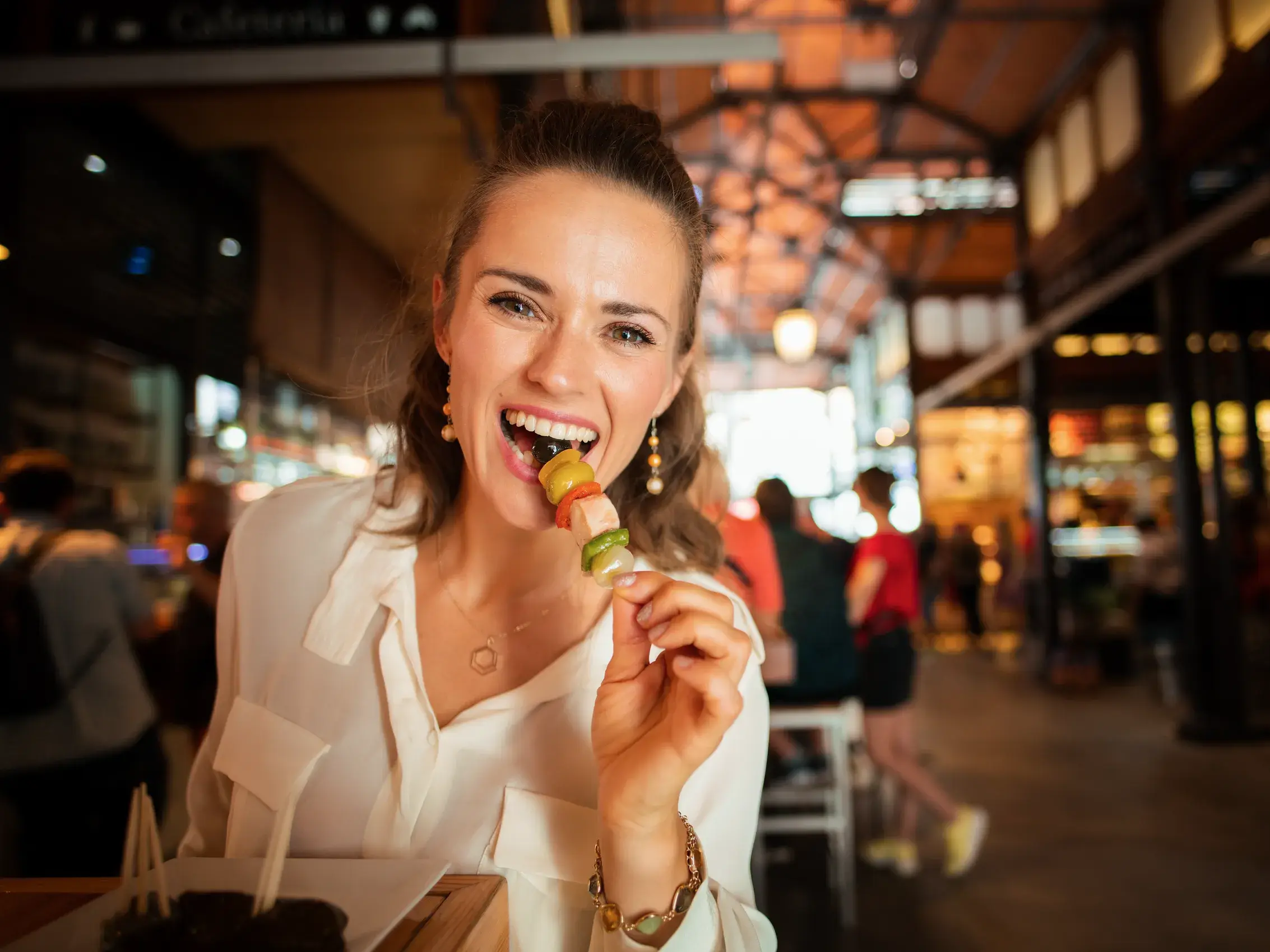 Eine fröhliche Frau probiert landestypische Tapas in einer belebten Markthalle während ihrer Andalusien-Reise.