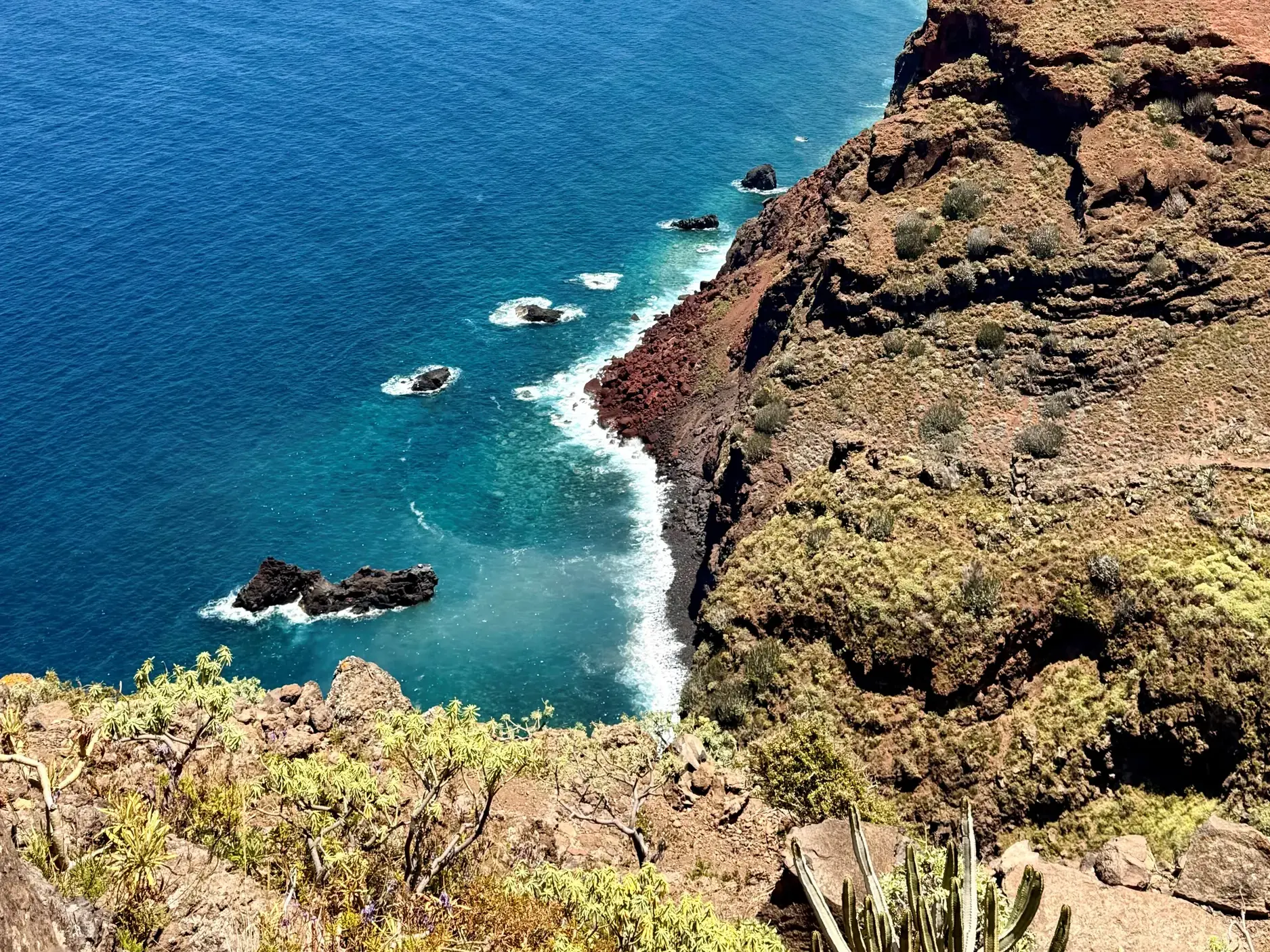 Blick von einem Wanderweg auf die steile Felsküste im Norden von La Palma mit tiefblauem Atlantik und Vulkanfelsen.
