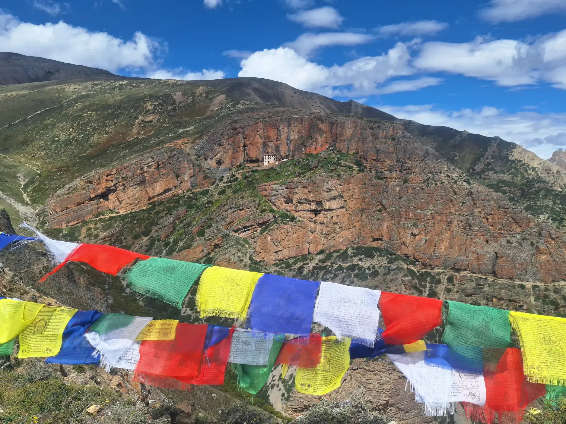Farbige tibetische Gebetsfahnen mit Blick auf das Kloster Tsakang Gompa in der Felswand während eines Trekkings im Inneren Dolpo.