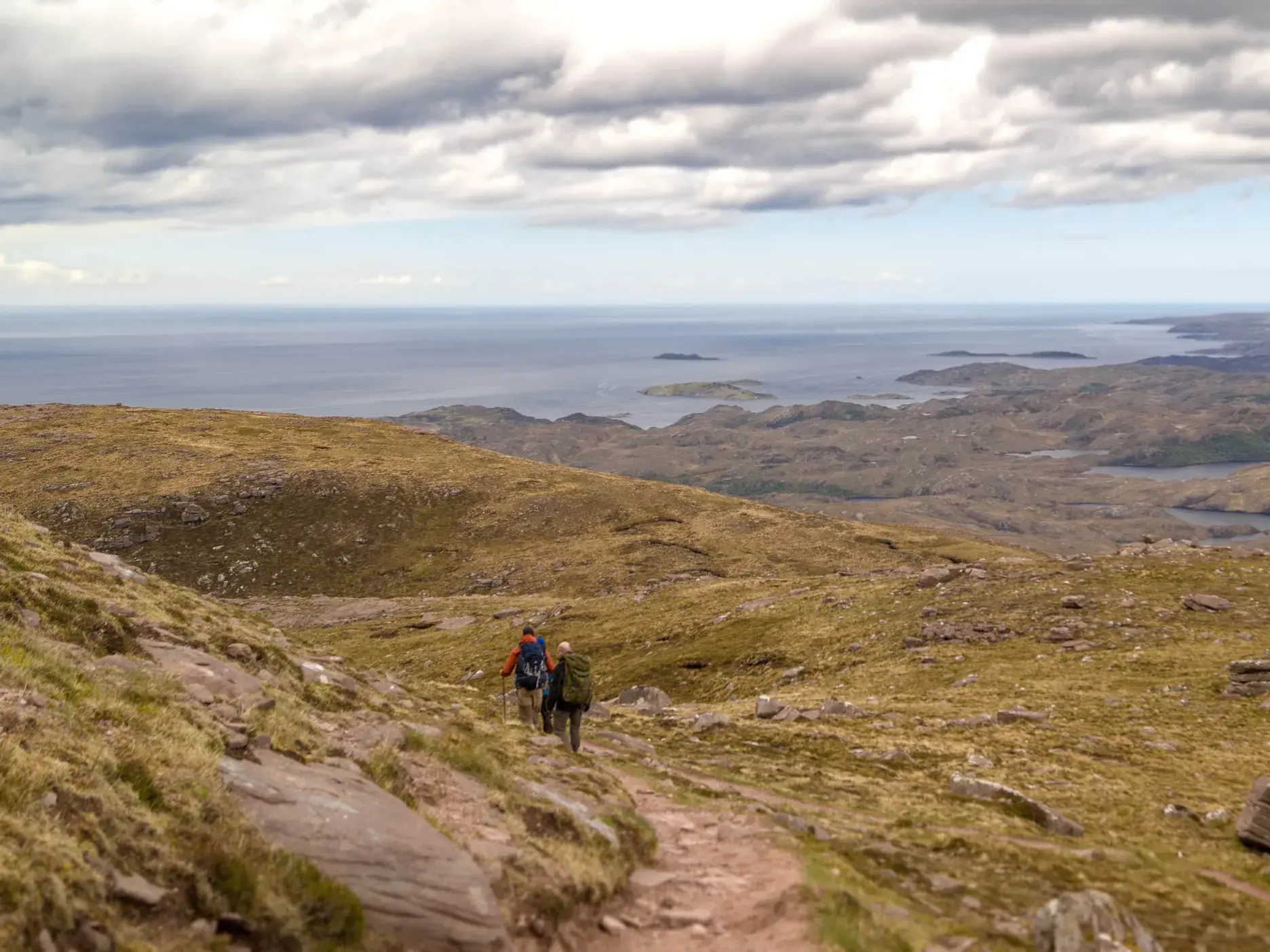 Zwei Wanderer auf einem Bergpfad in der Region Wester Ross mit Panoramablick über die North West Highlands Schottlands.