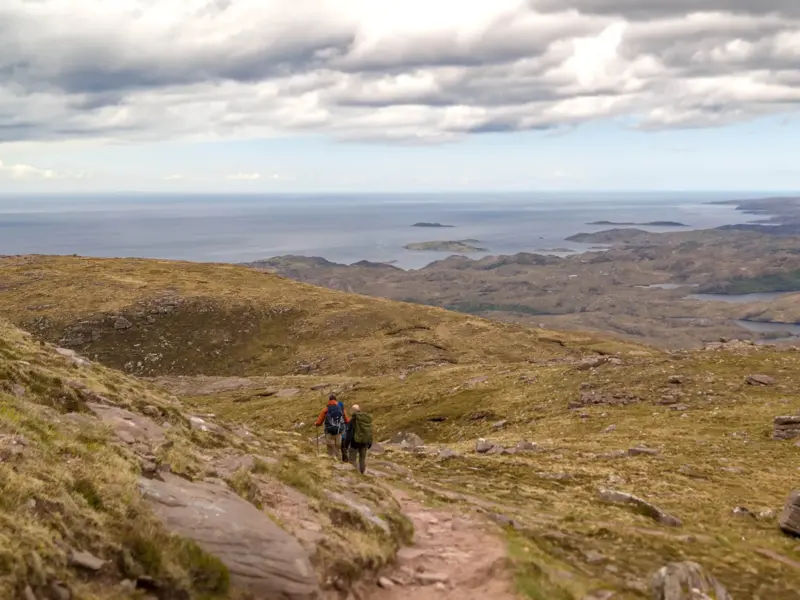 Zwei Wanderer auf einem Bergpfad in der Region Wester Ross mit Panoramablick über die North West Highlands Schottlands.
