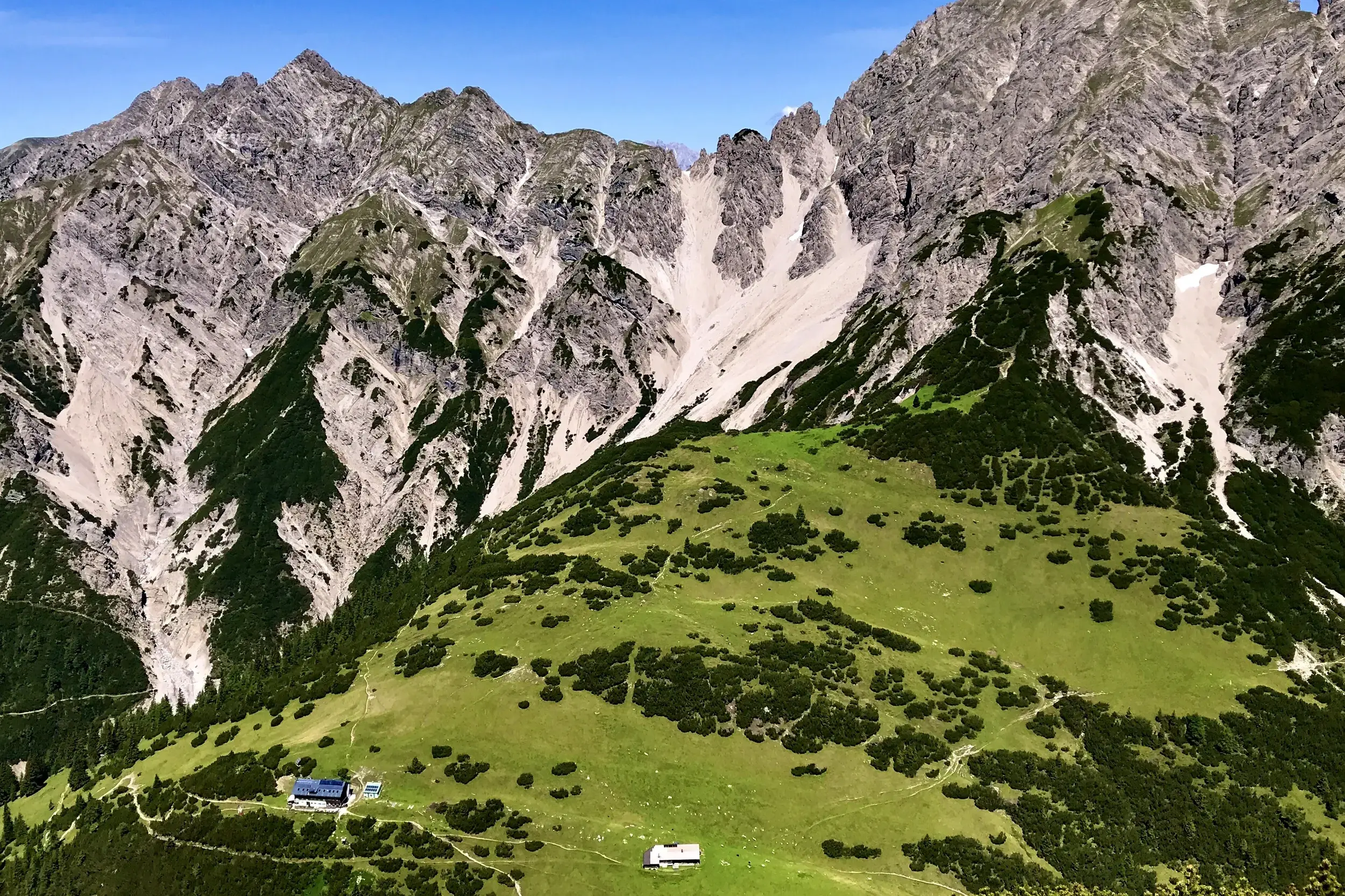 Die idyllisch gelegene Eppzirler Alm auf grünen Hängen vor der markanten Kulisse der Erlspitzgruppe im Karwendel.