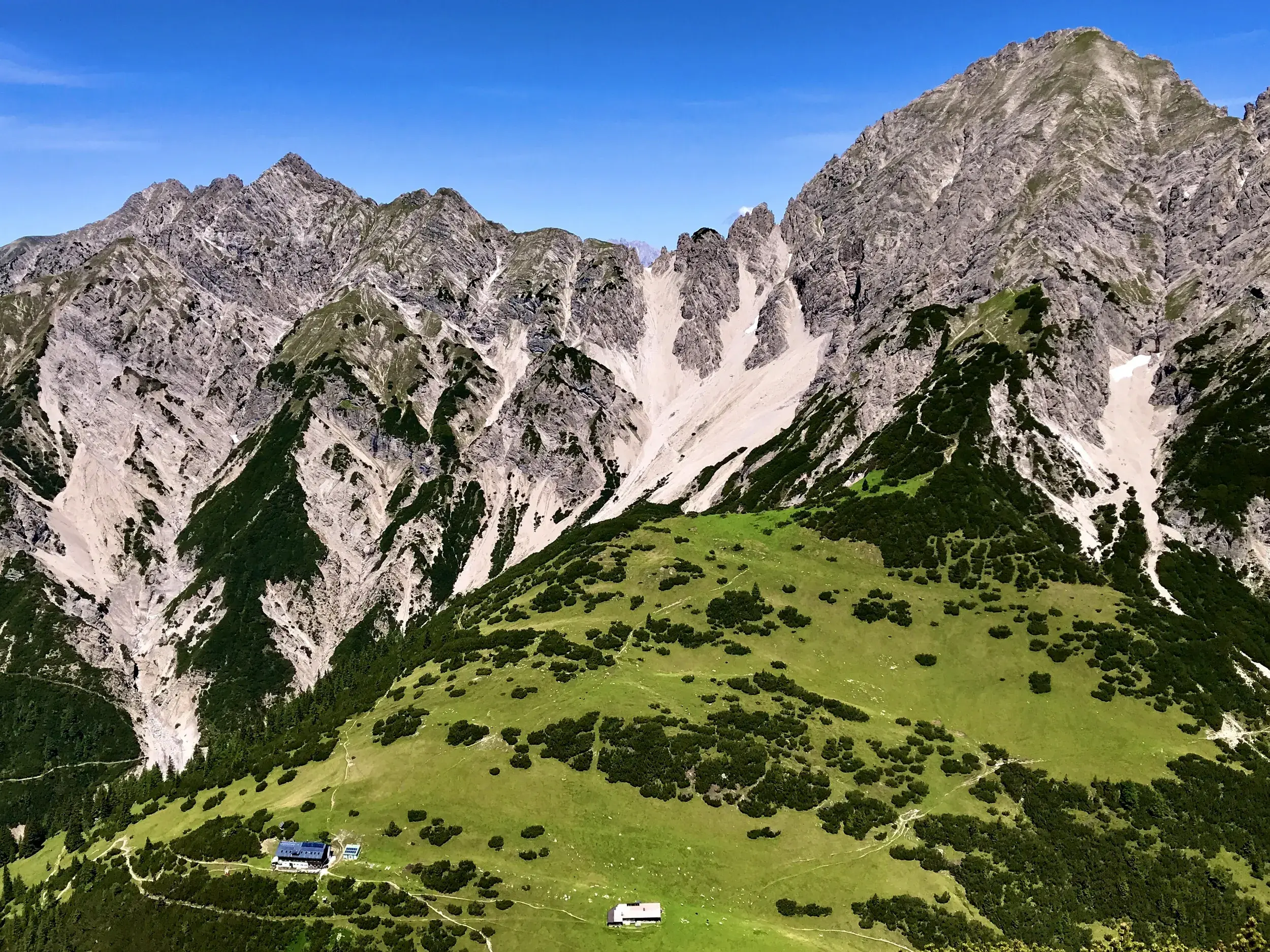 Die idyllisch gelegene Eppzirler Alm auf grünen Hängen vor der markanten Kulisse der Erlspitzgruppe im Karwendel.