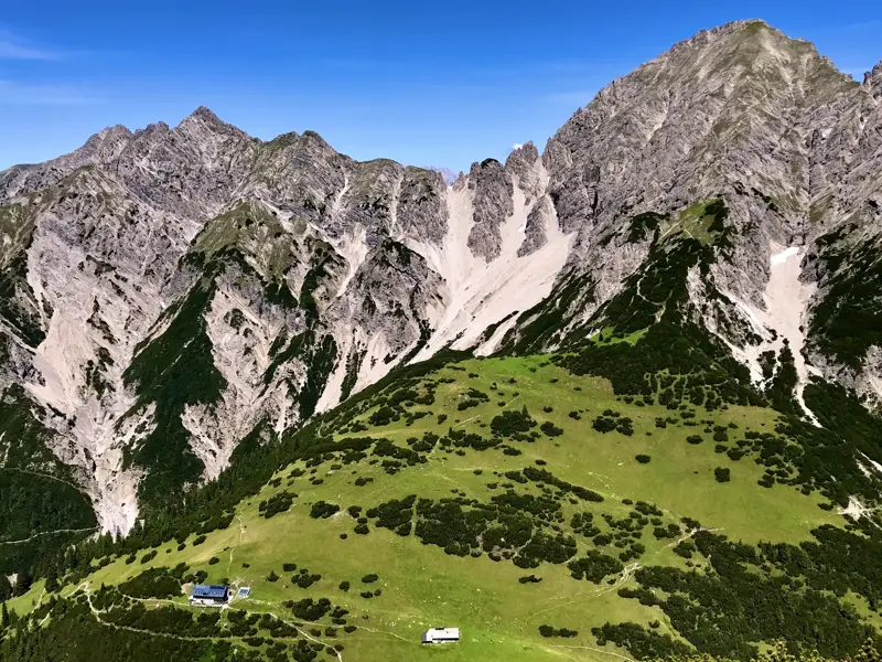 Die idyllisch gelegene Eppzirler Alm auf grünen Hängen vor der markanten Kulisse der Erlspitzgruppe im Karwendel.